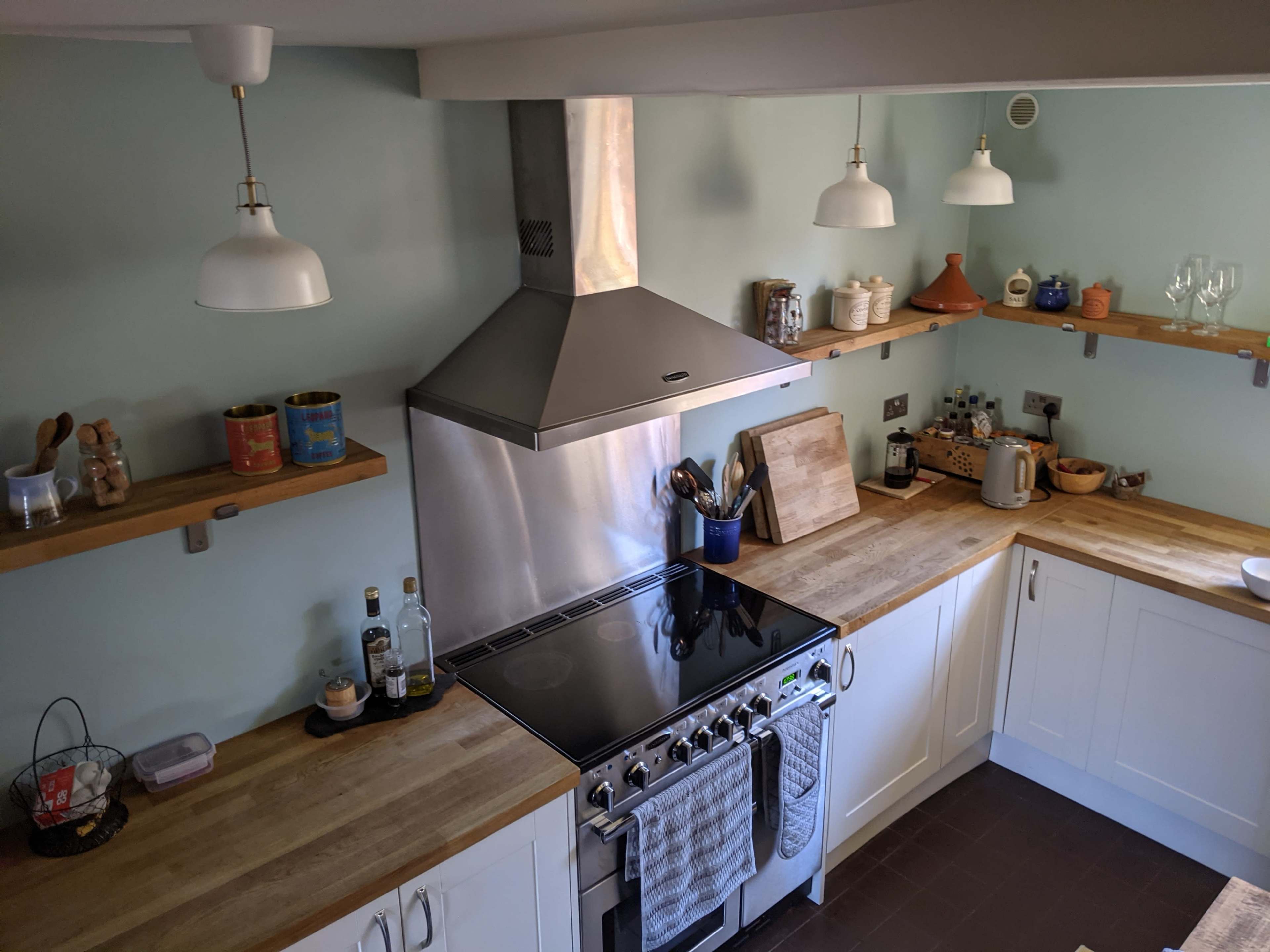 A modern kitchen with a stainless steel hood over a gas stove, wooden countertops, and light green walls.