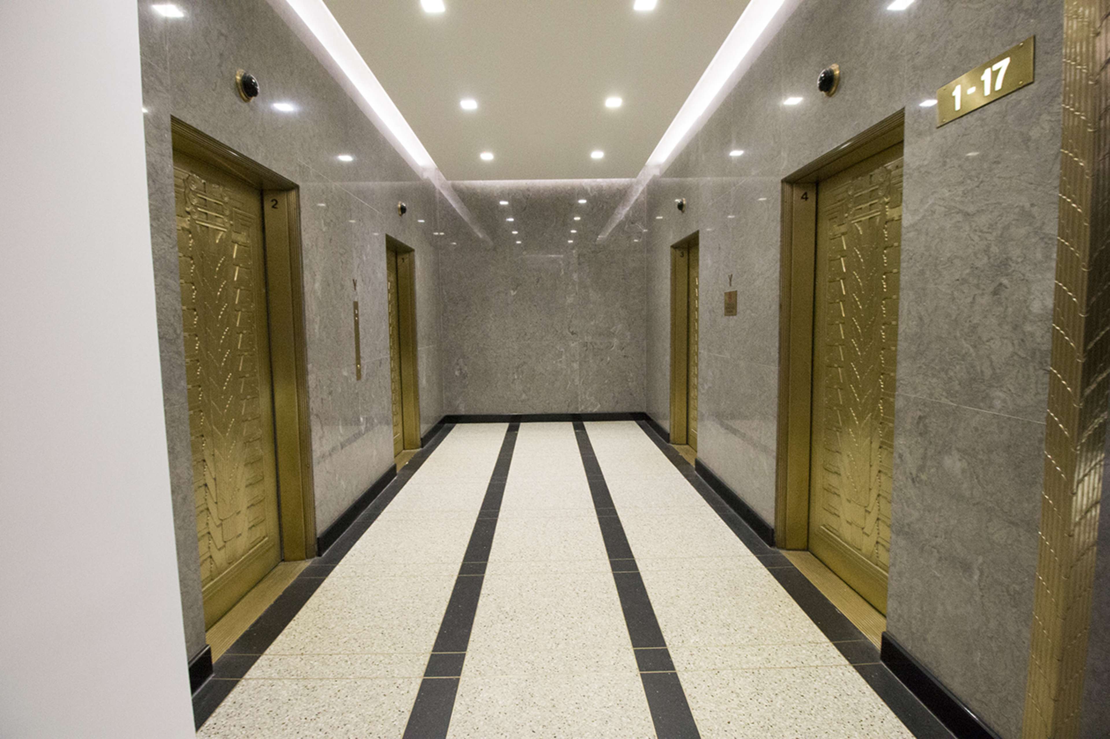 A well-lit lobby area with three gold-colored elevators against a marble backdrop and a patterned floor.