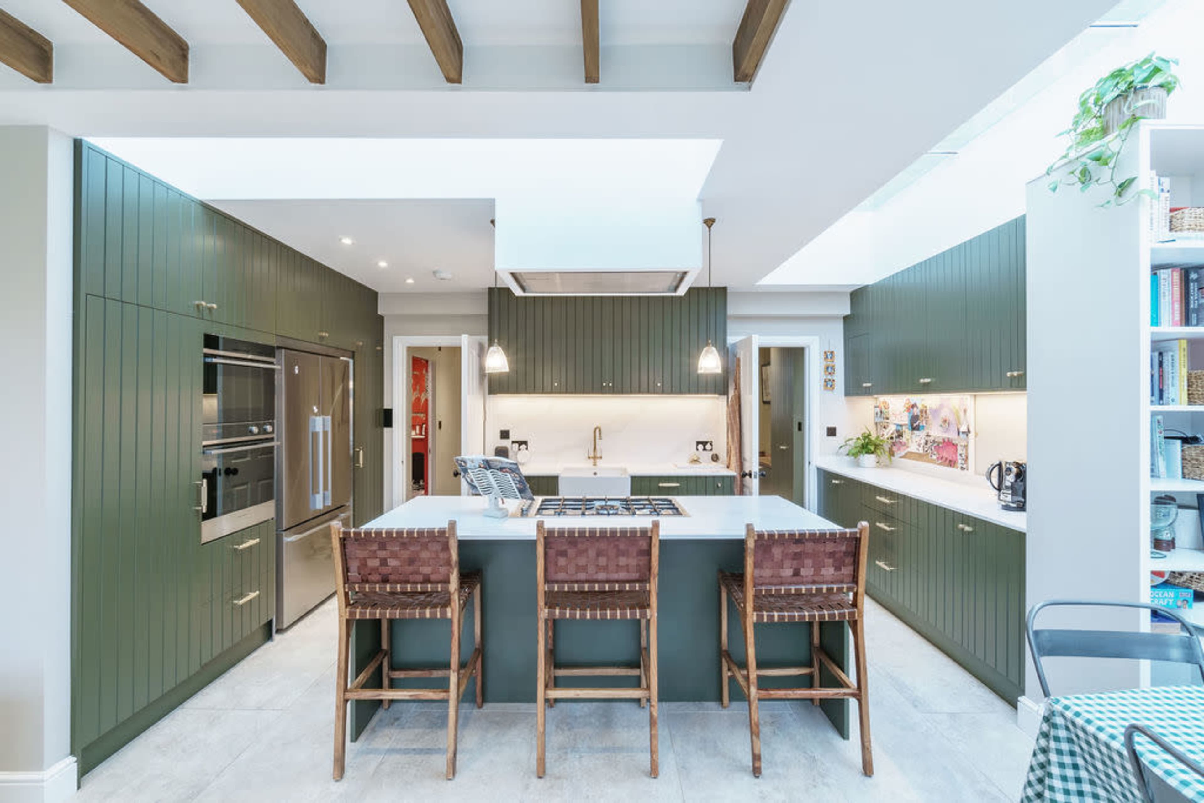 A modern kitchen with green cabinetry, a central island with a cooktop, and three wooden stools.