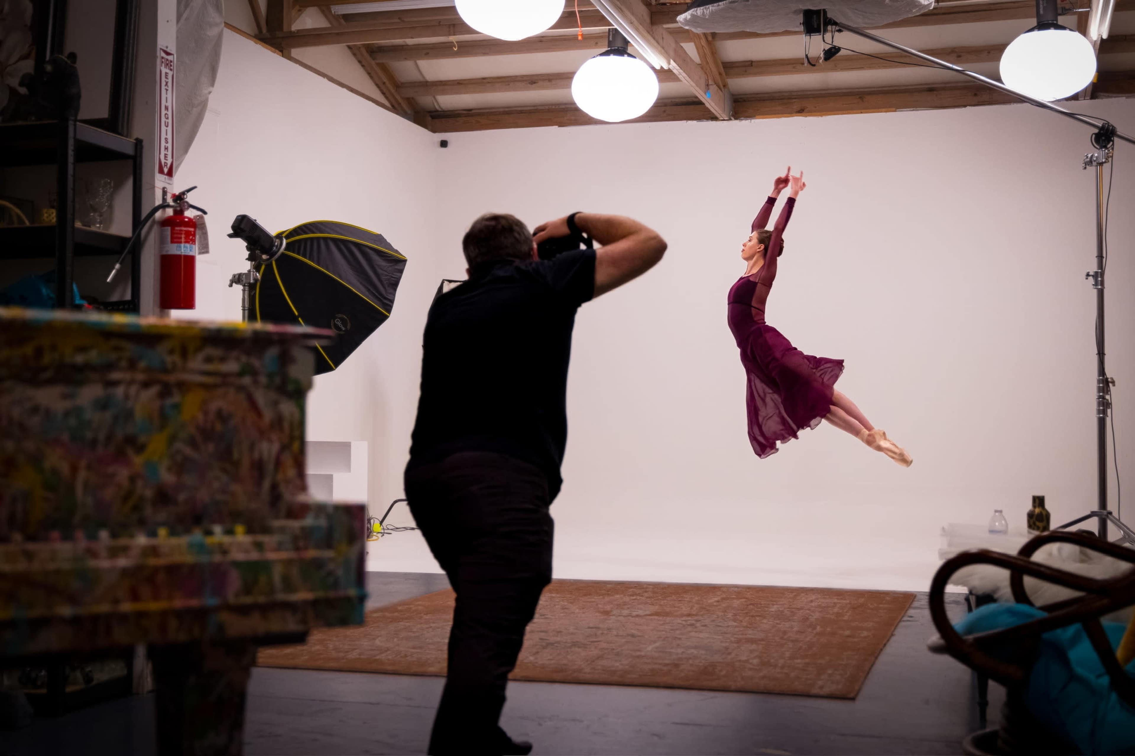 A dancer leaps gracefully in mid-air while a photographer captures the moment in a studio setting.