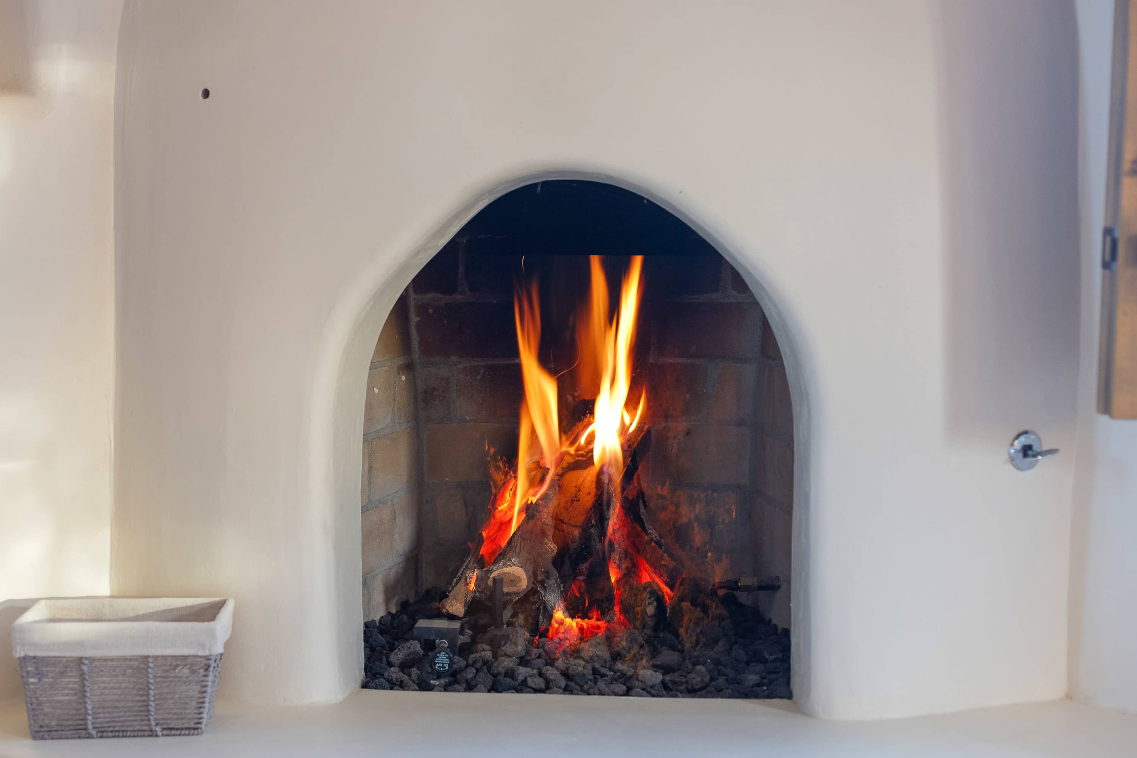 A fire burns in a brick fireplace with a curved arch, surrounded by a light-colored wall.