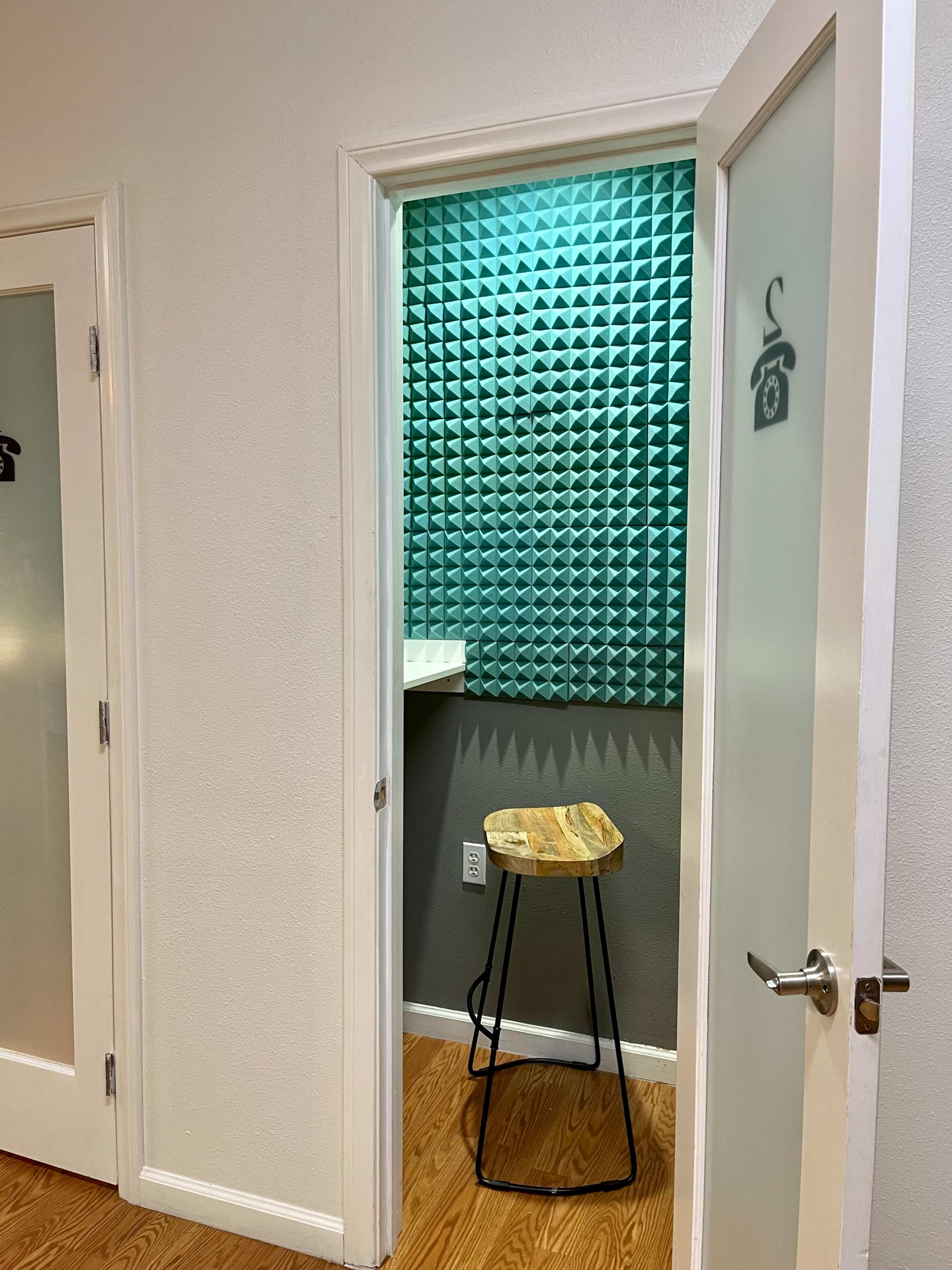 An open door leading to a small room with green acoustic panels, a wooden stool, and a countertop.