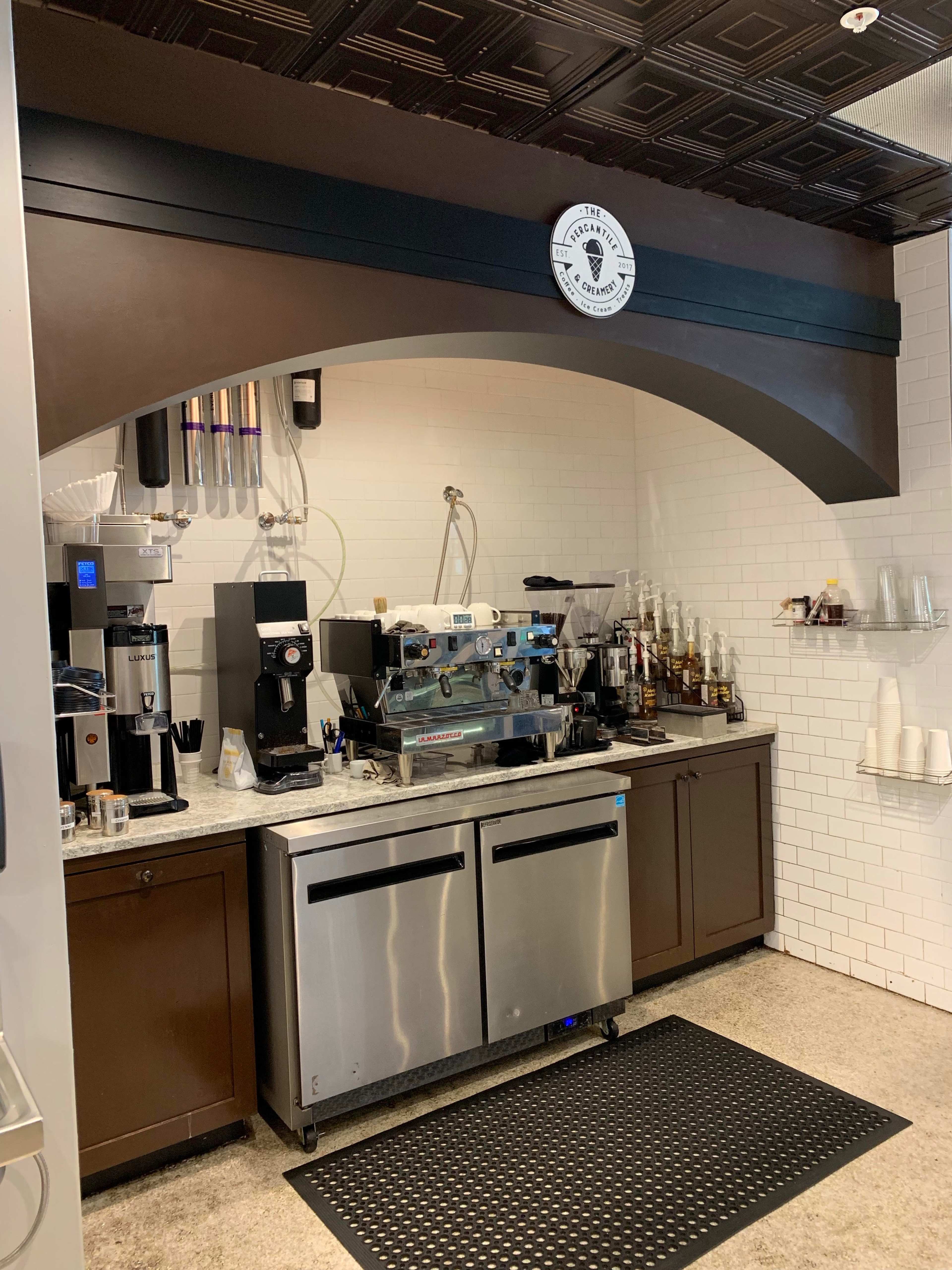 A coffee shop counter with an espresso machine, coffee grinders, and a variety of drink ingredients arranged behind a sleek marble surface.