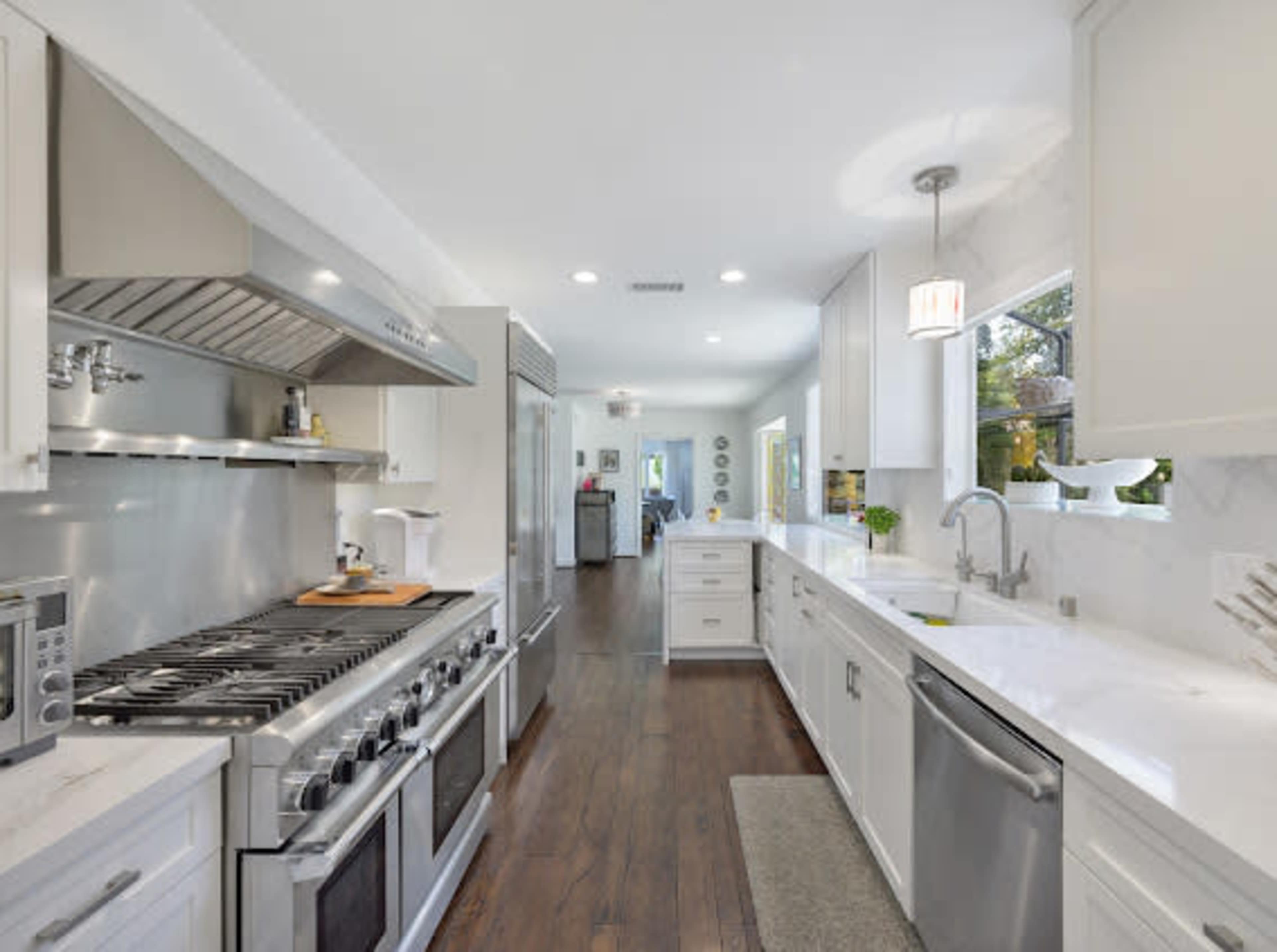 A modern kitchen features stainless steel appliances, white cabinetry, and a central island with a gas stove.