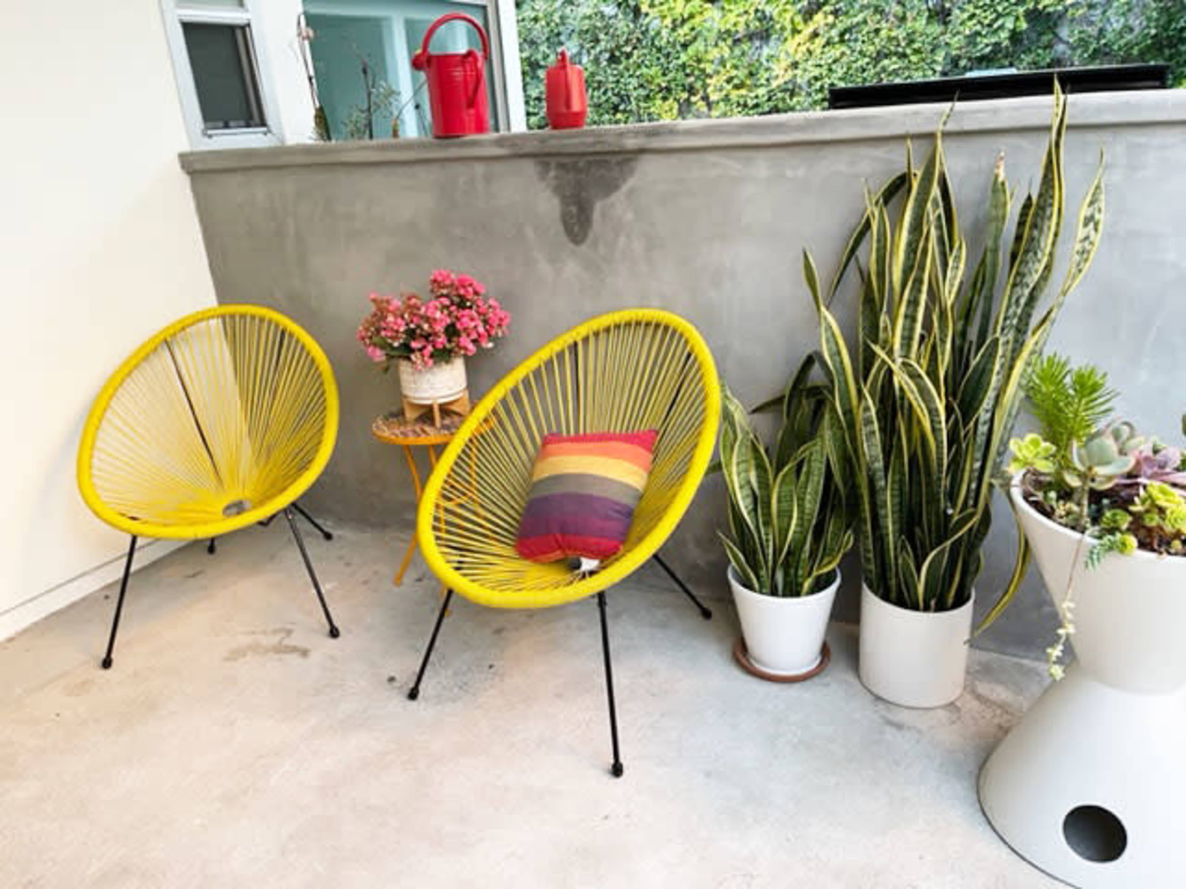 Two yellow chairs next to a small table with flowers, surrounded by potted plants in a brightly lit outdoor space.