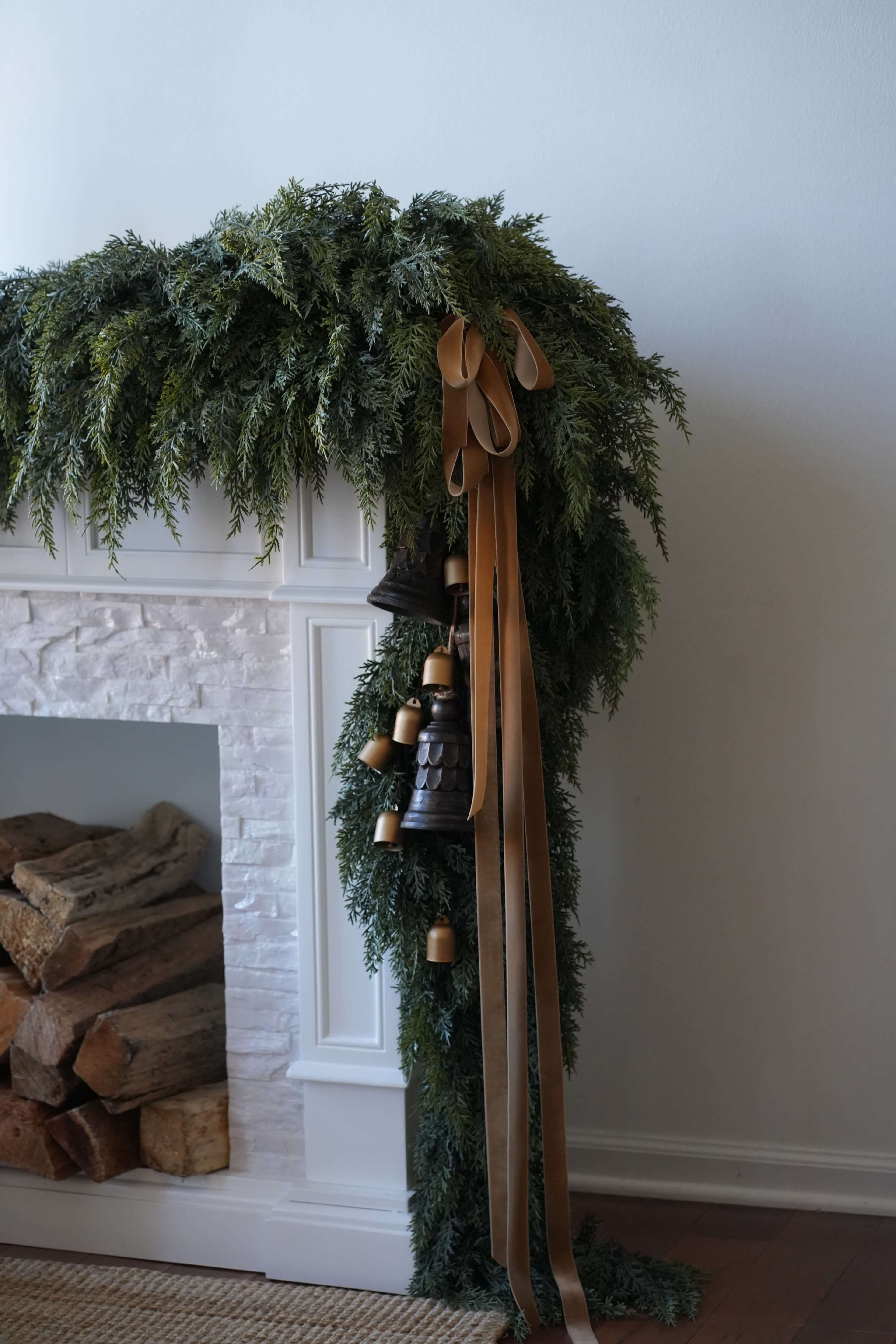 A garland of greenery drapes over a white mantelpiece, accented with golden ribbons and decorative bells.
