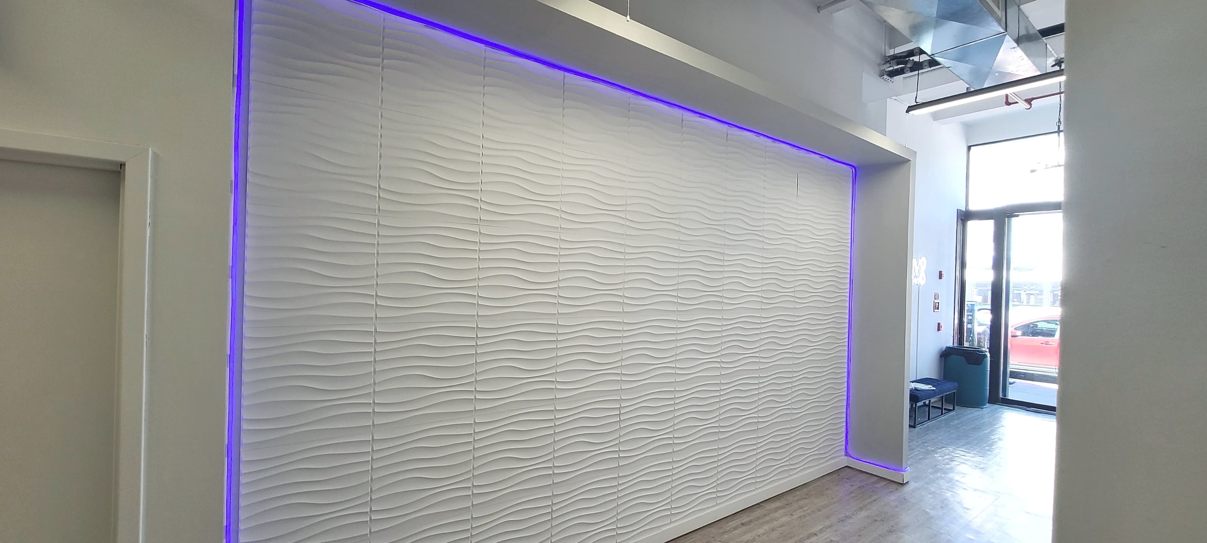 A textured white wall with wave patterns is illuminated by a purple light, and a glass door leads to the outside.