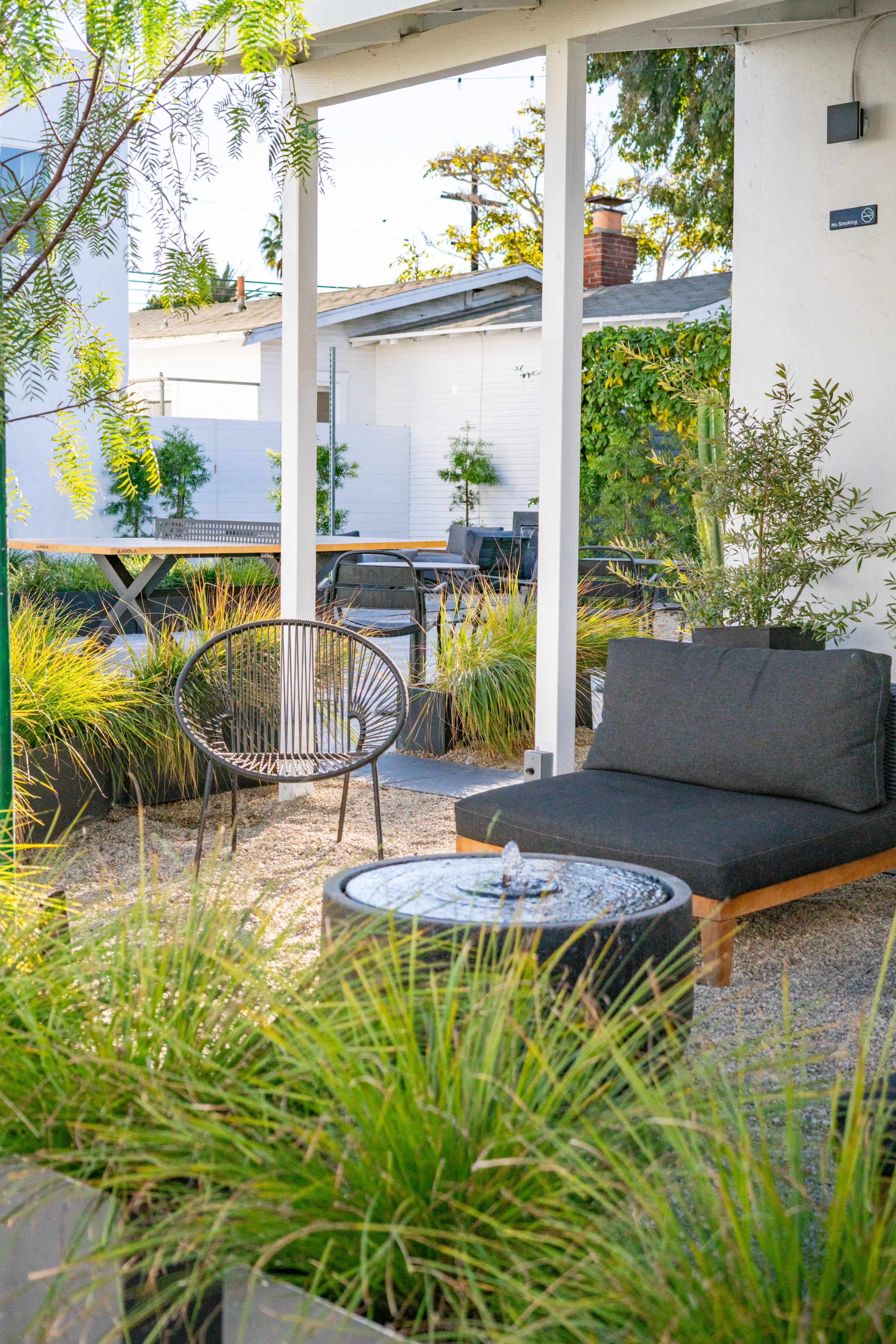The image shows a modern outdoor seating area with a black cushioned chair and a low table surrounded by decorative plants.