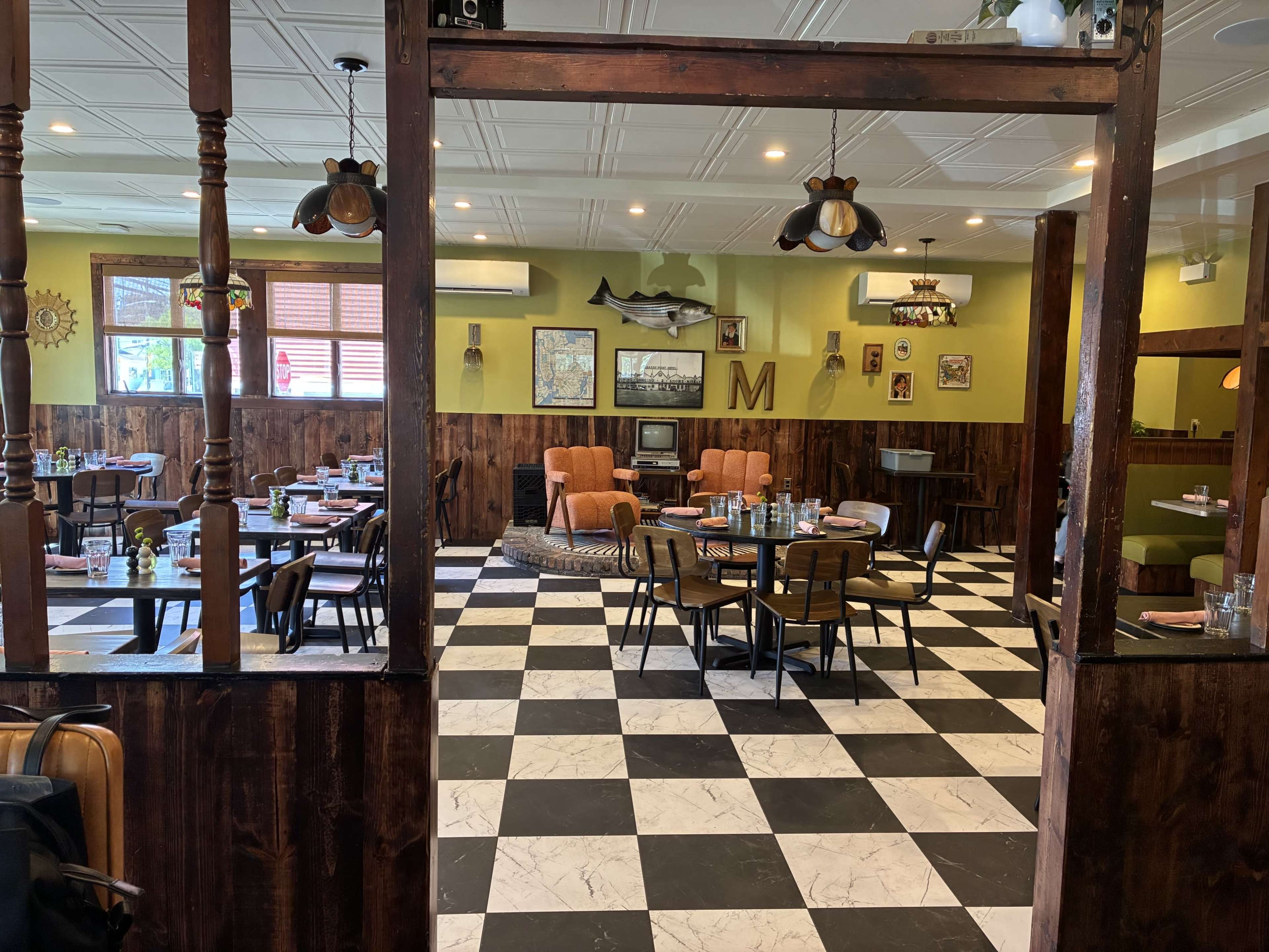 The image shows a restaurant interior with checkered flooring, wooden paneling, and vintage décor, featuring tables set for dining and bright green walls.