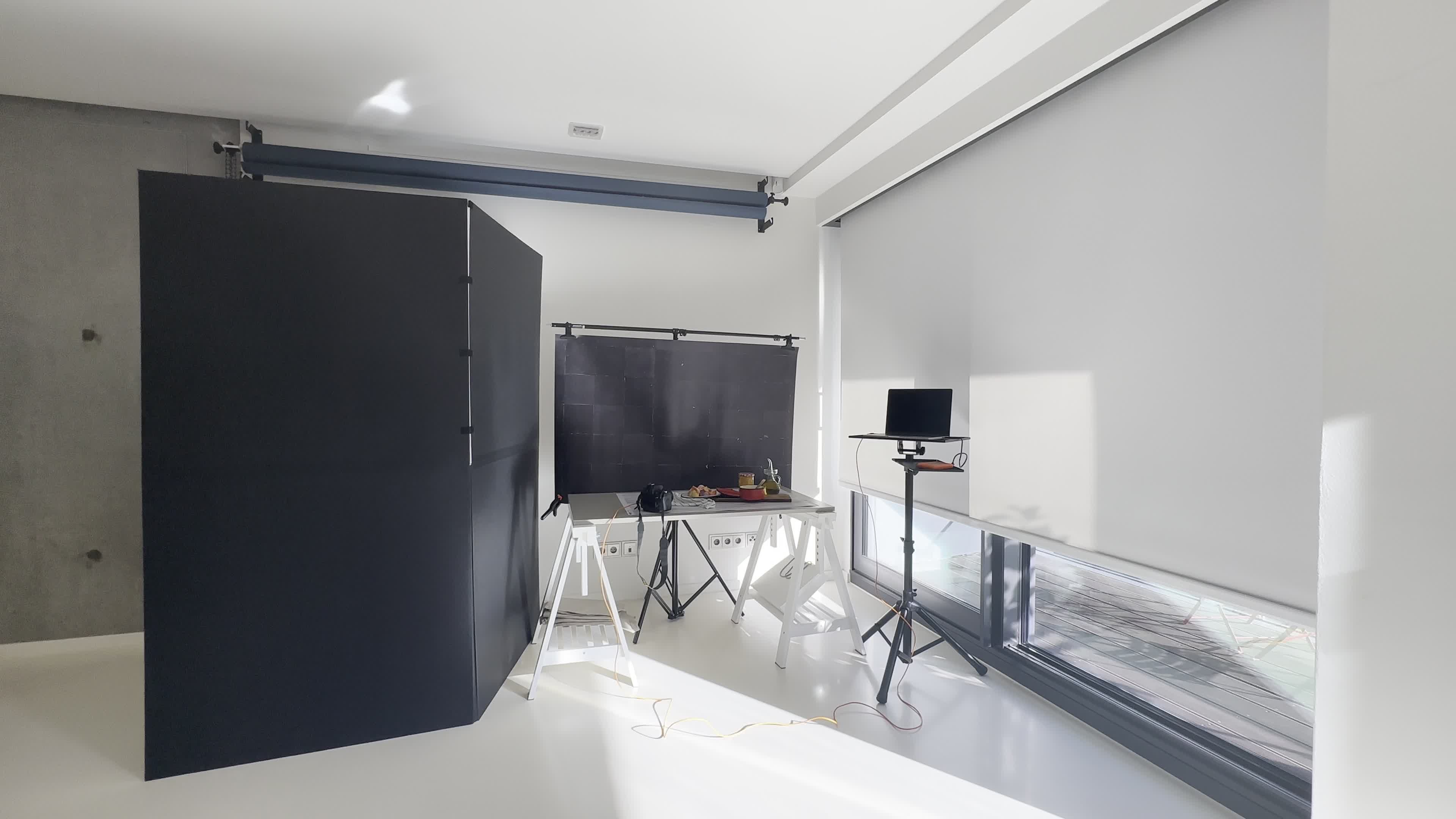 A modern interior space with a gray backdrop, work tables, and a large window letting in natural light.