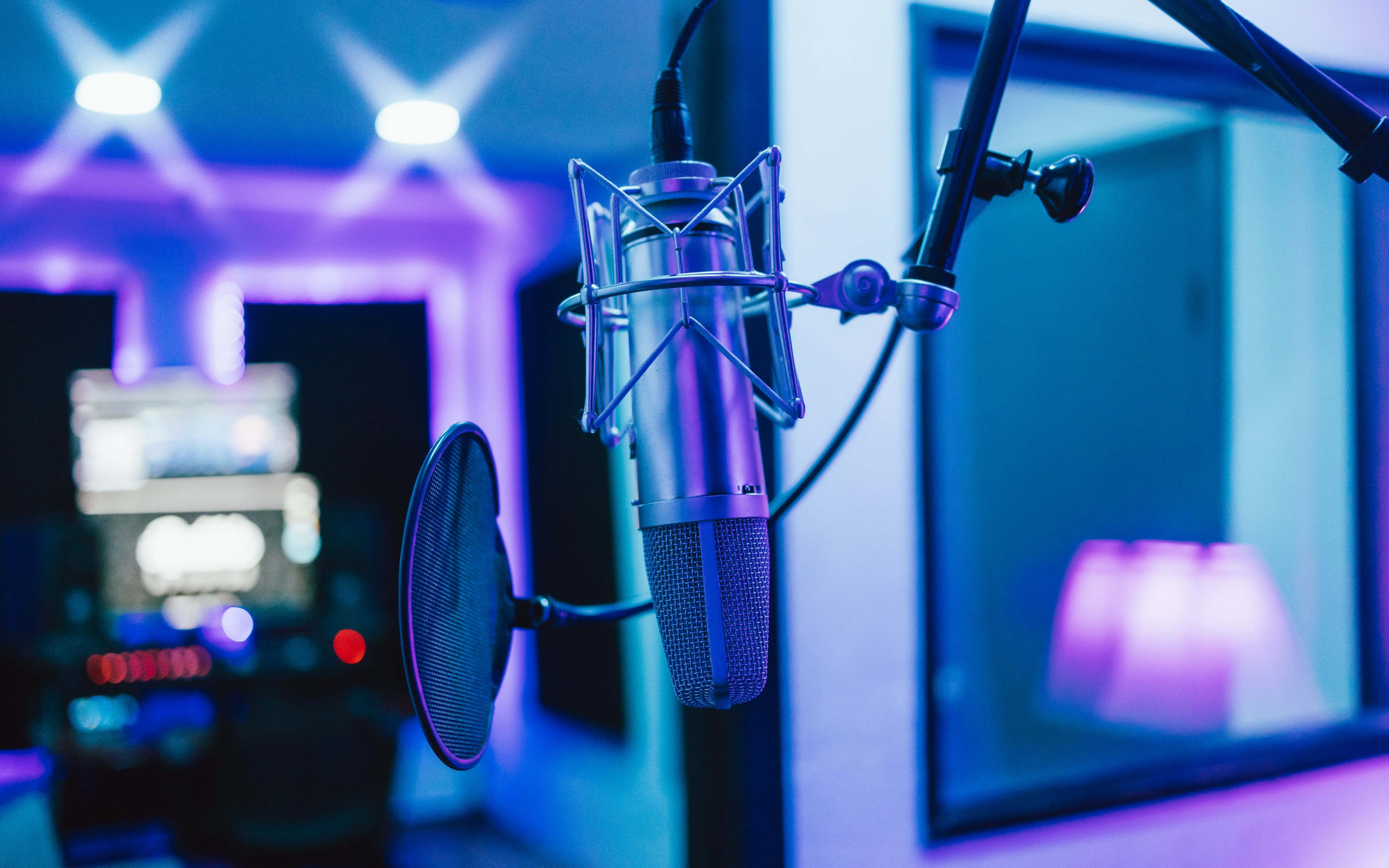 A microphone is positioned in a recording studio with ambient blue lighting and equipment visible in the background.