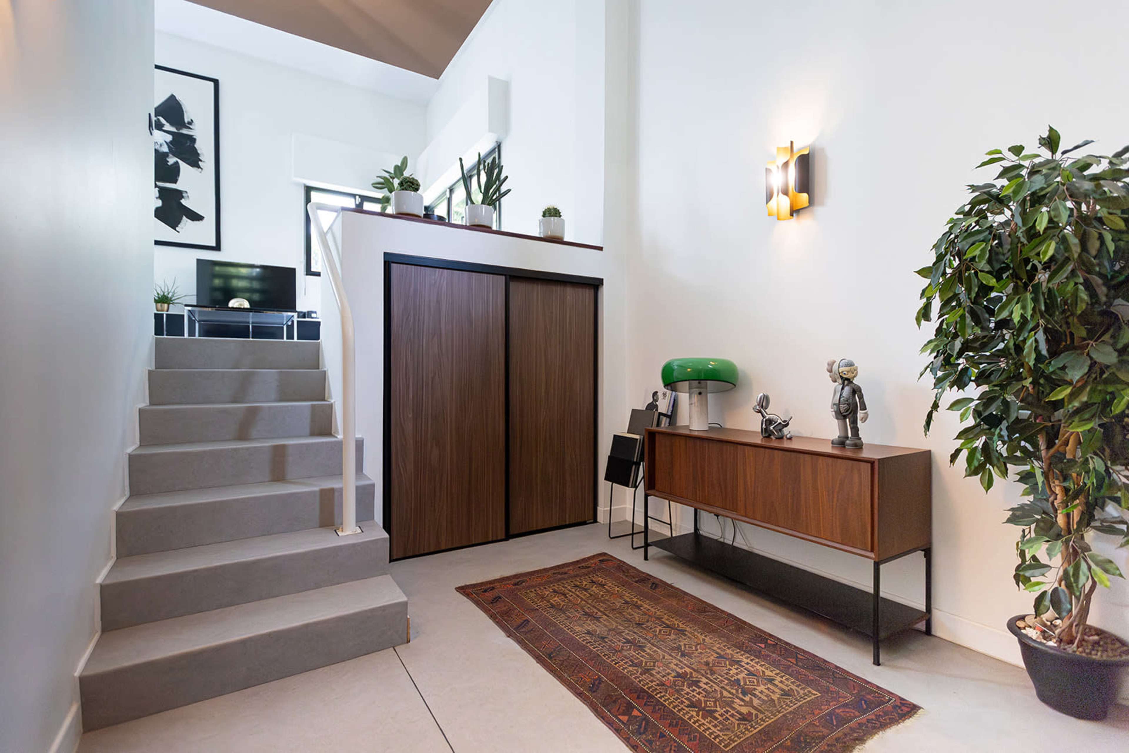 A modern entryway featuring a staircase, a console table with decorative items, and plants beside a large closet.