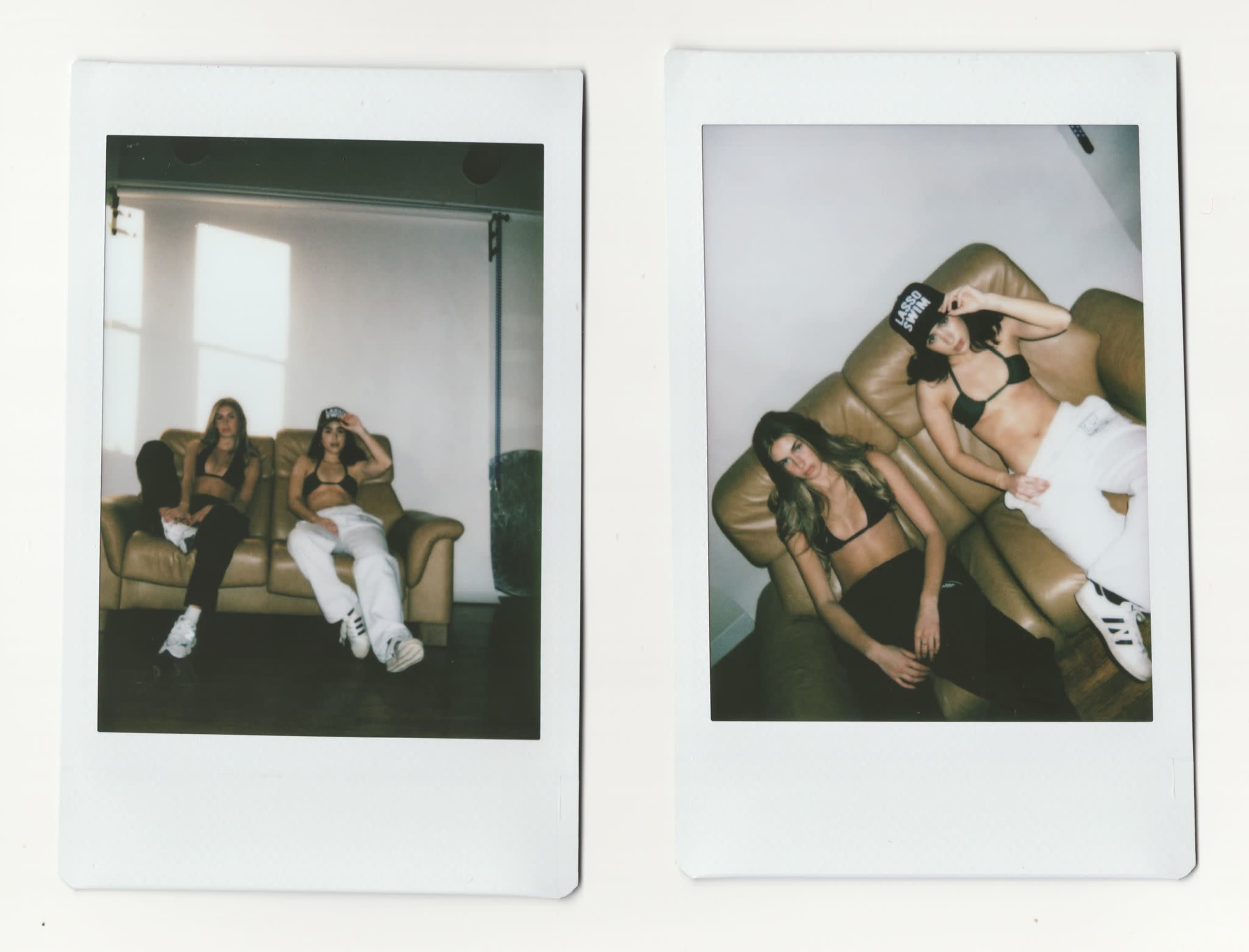 Two women are lounging on a brown sofa in a well-lit room, wearing casual clothing and hats.