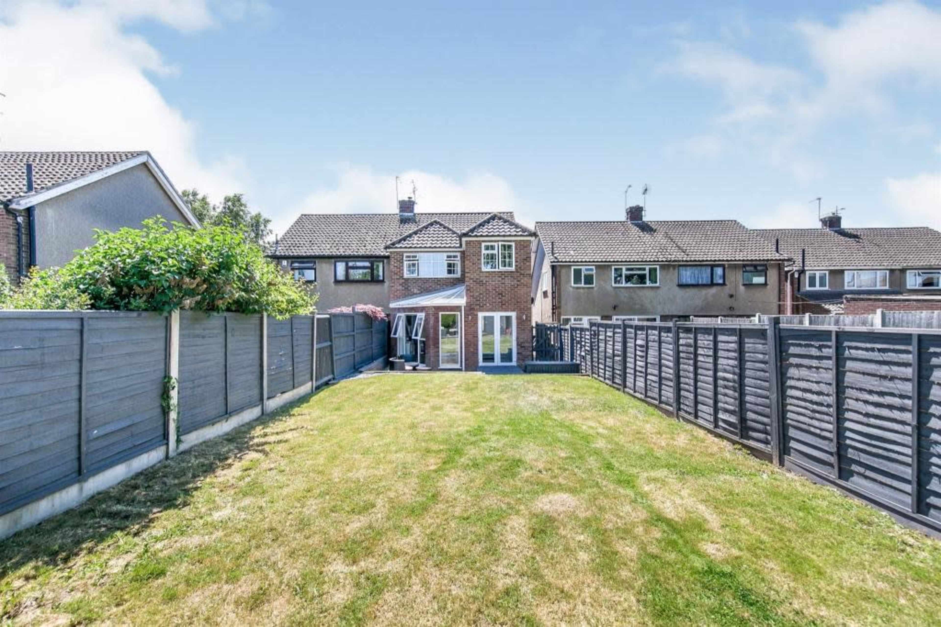 A two-story brick house with a backyard featuring a grassy area and wooden fencing on both sides.