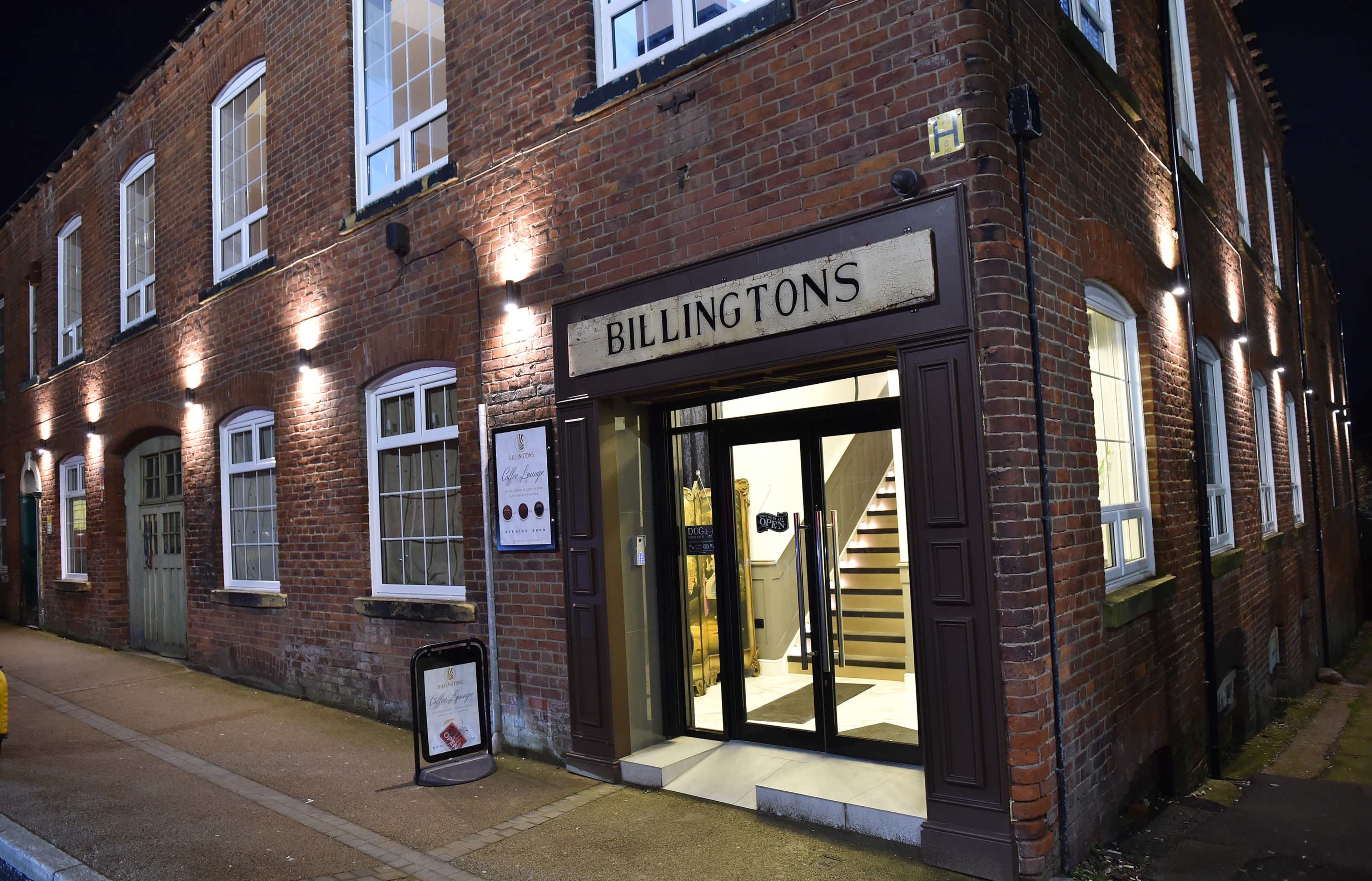 The image shows the exterior of a brick building with large windows and a sign that reads "BILLINGTONS," featuring an entrance with glass doors.