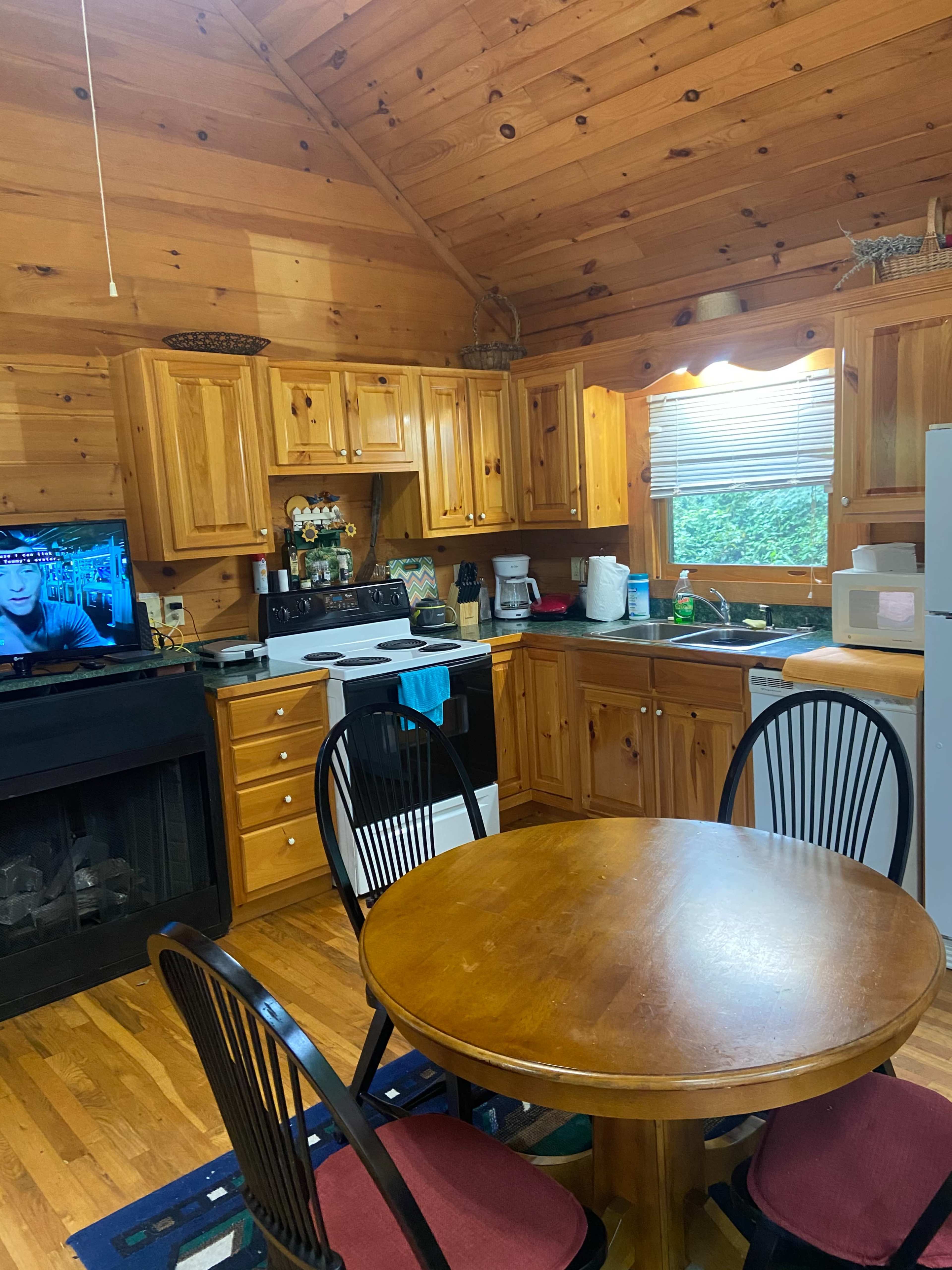 The image shows a wooden kitchen with cabinets, a dining table, and appliances, including a stove, refrigerator, and microwave.