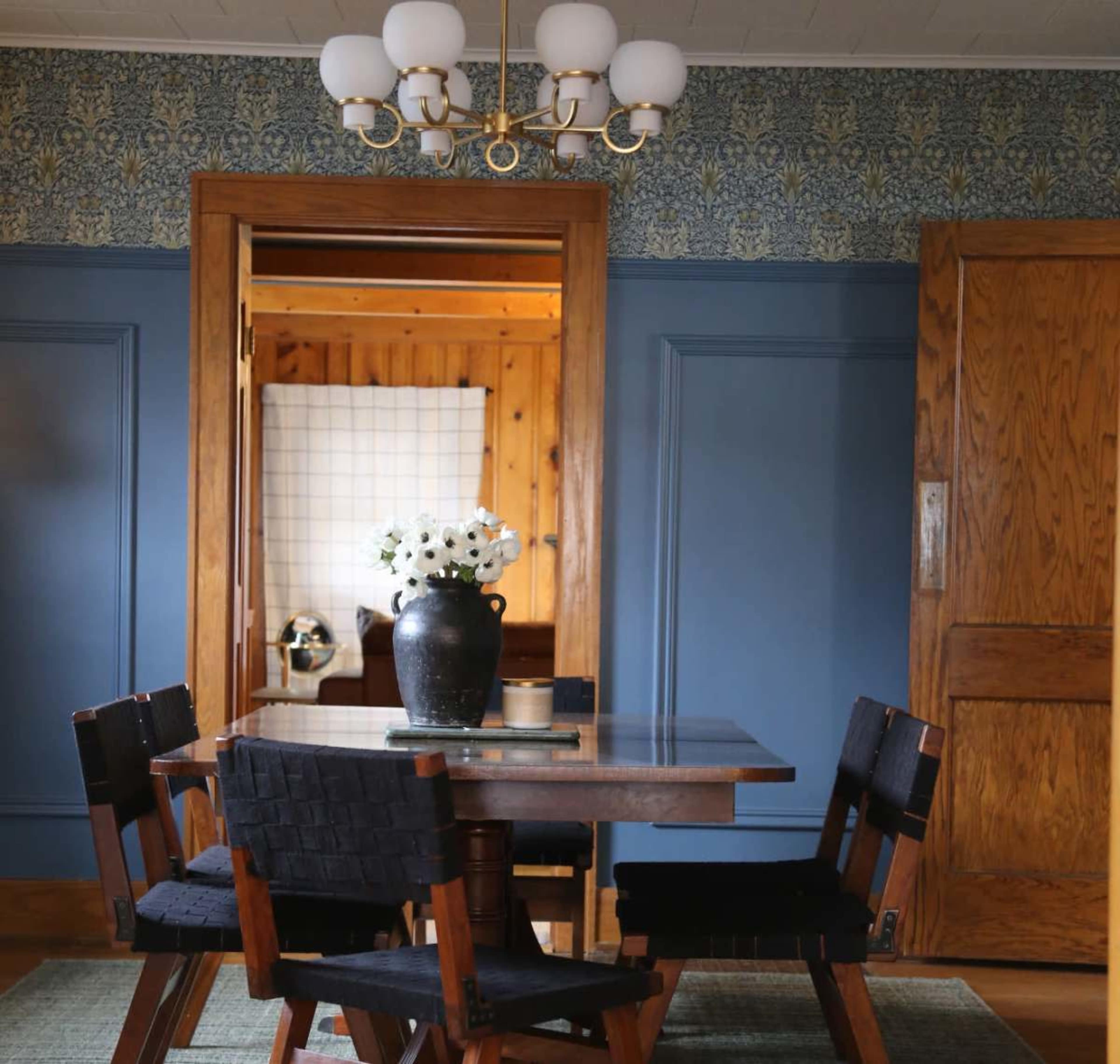 A wooden dining table surrounded by black chairs is set in a room with blue walls and a patterned wallpaper.
