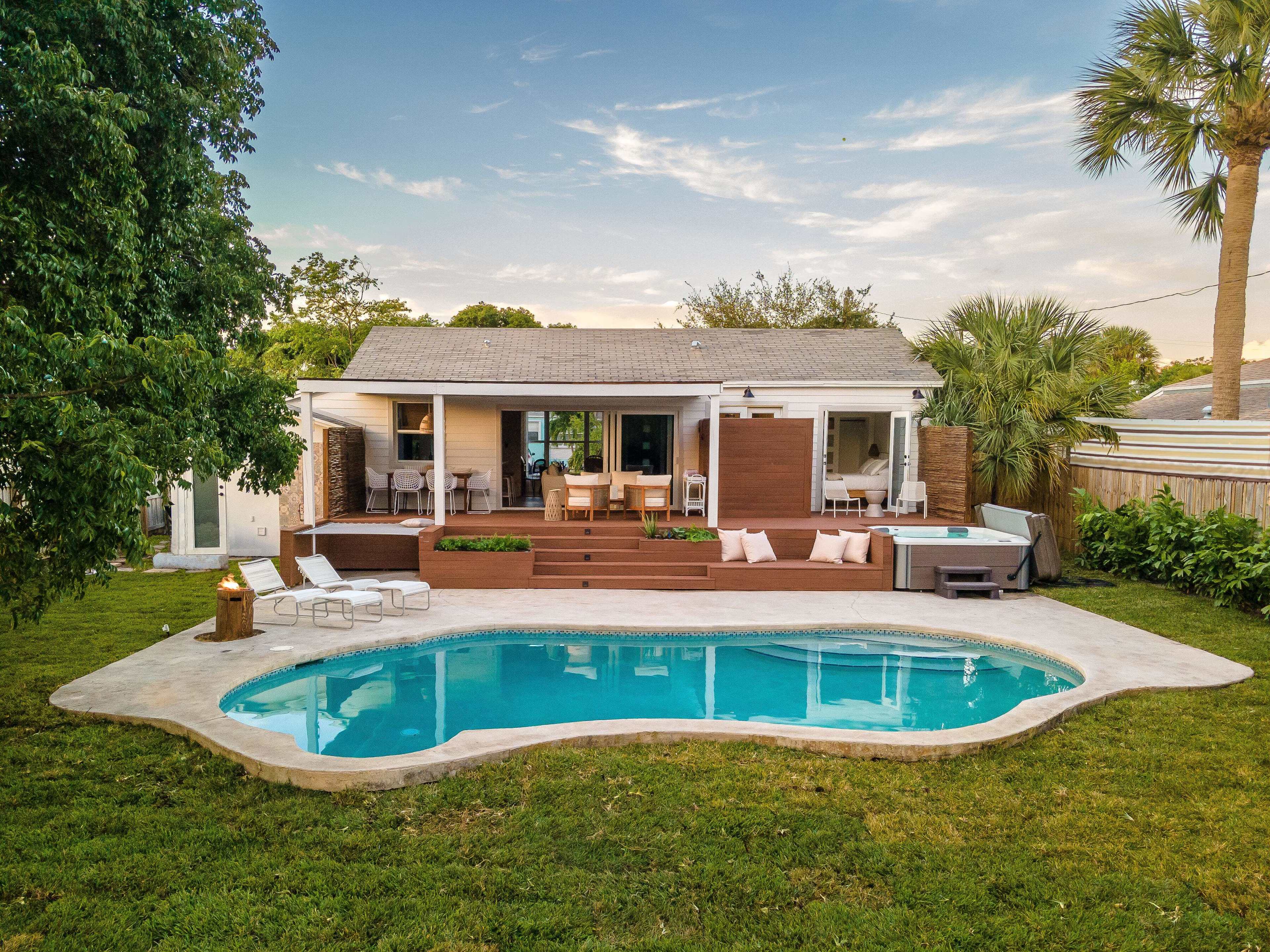 A single-story house with a backyard pool is surrounded by lawn furniture and palm trees.