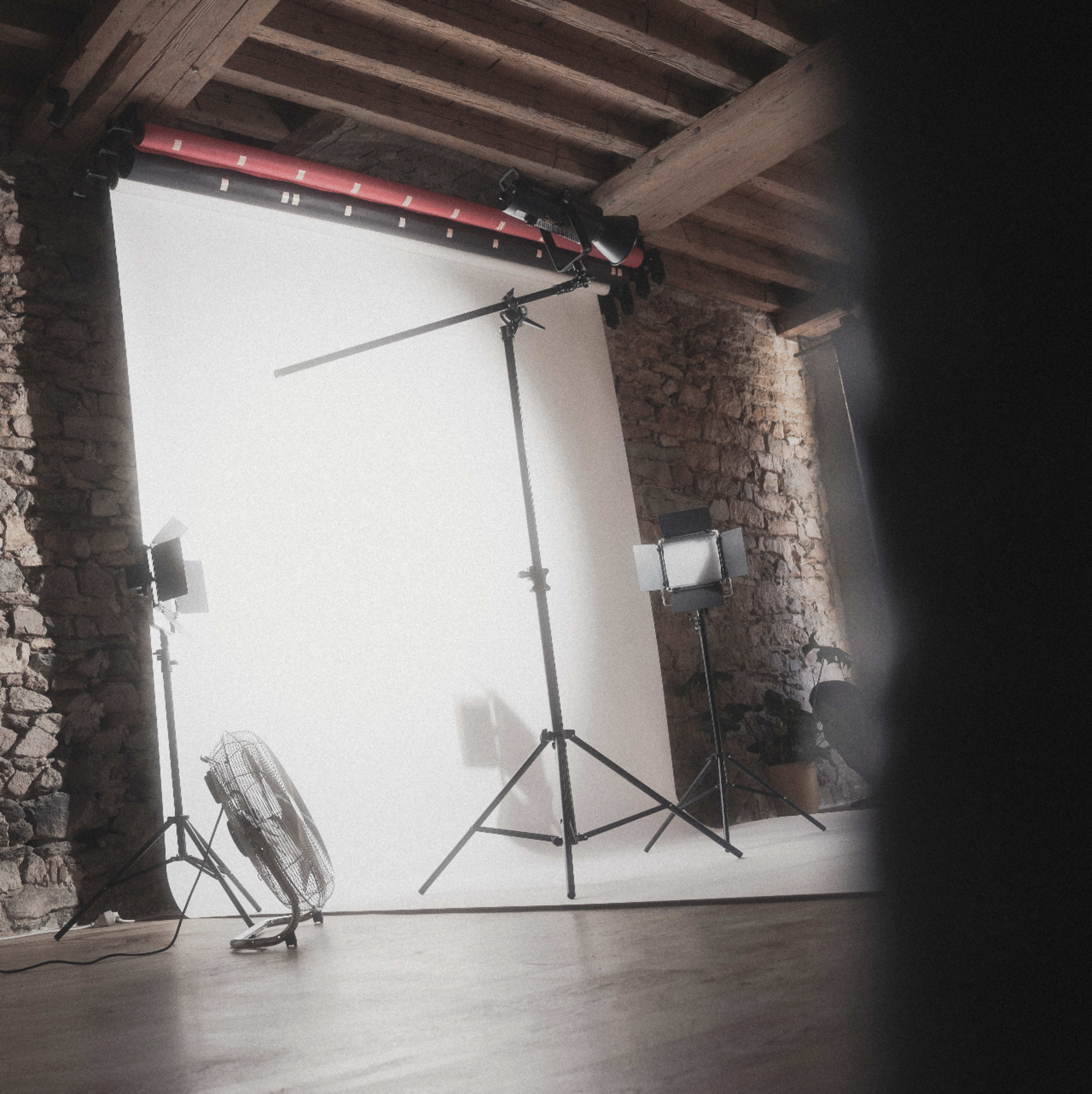 The image shows a photography studio with a blank backdrop, lighting equipment, and a fan positioned on the floor.