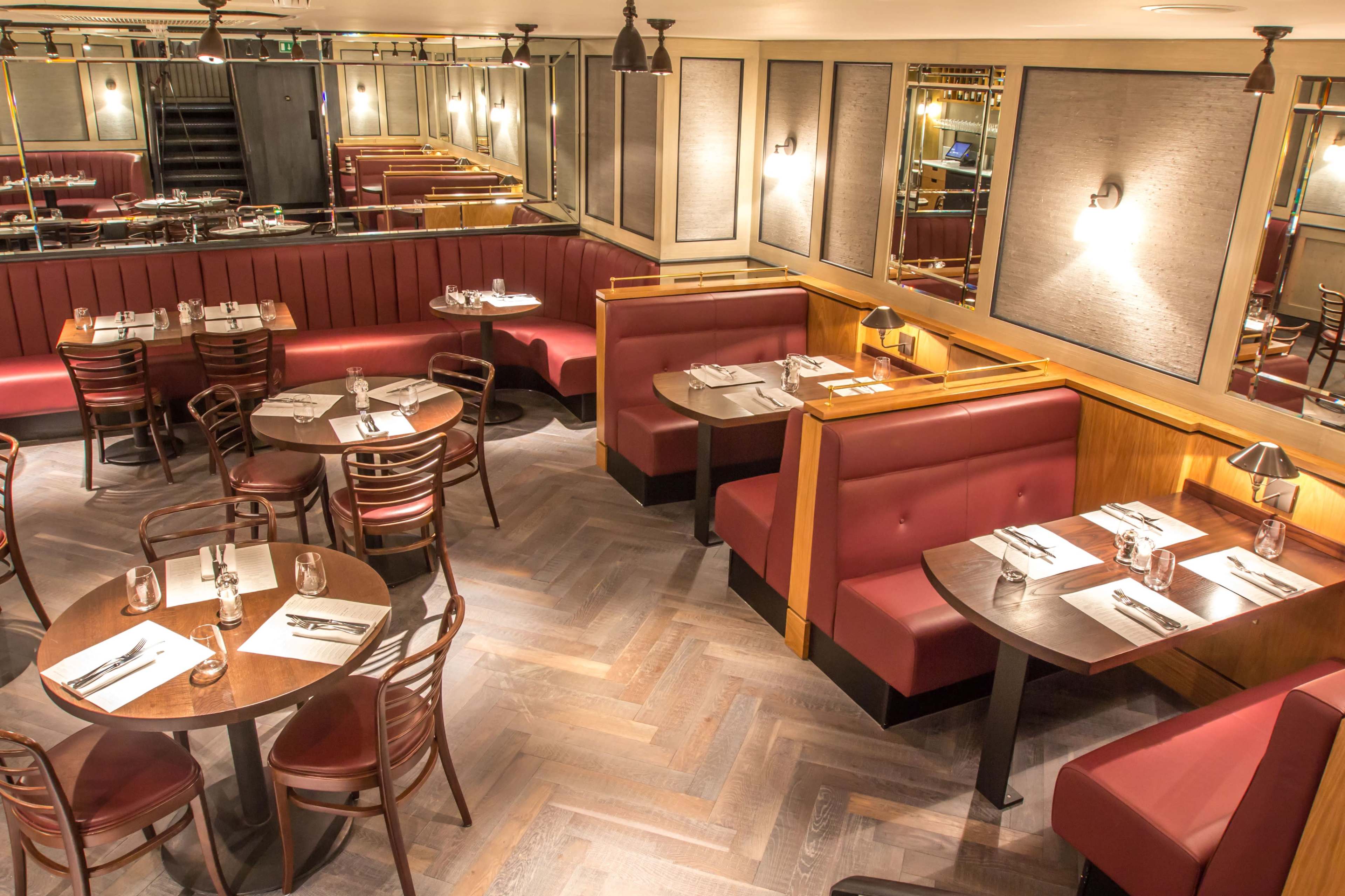 The image shows a warmly lit restaurant interior featuring red leather booths and wooden tables arranged around a polished wood floor.