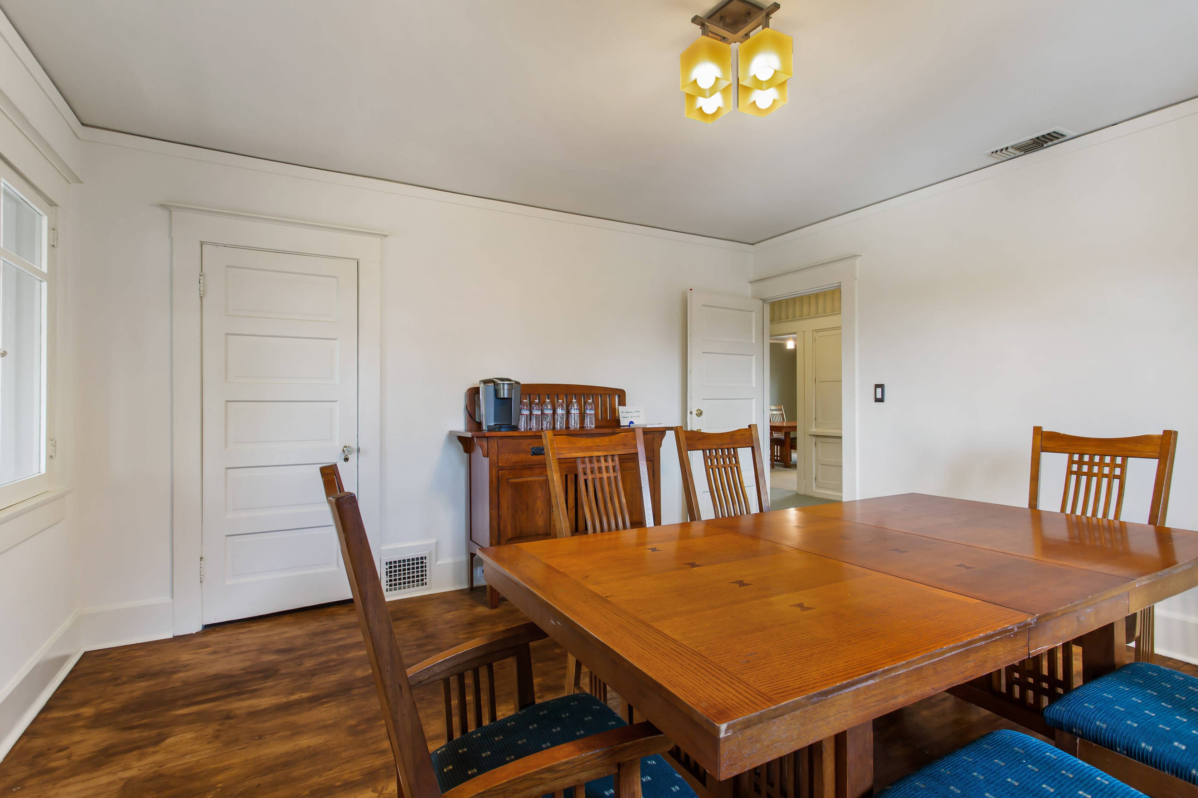 A dining room with a wooden table surrounded by chairs, a sideboard, and a closed door leading to another room.
