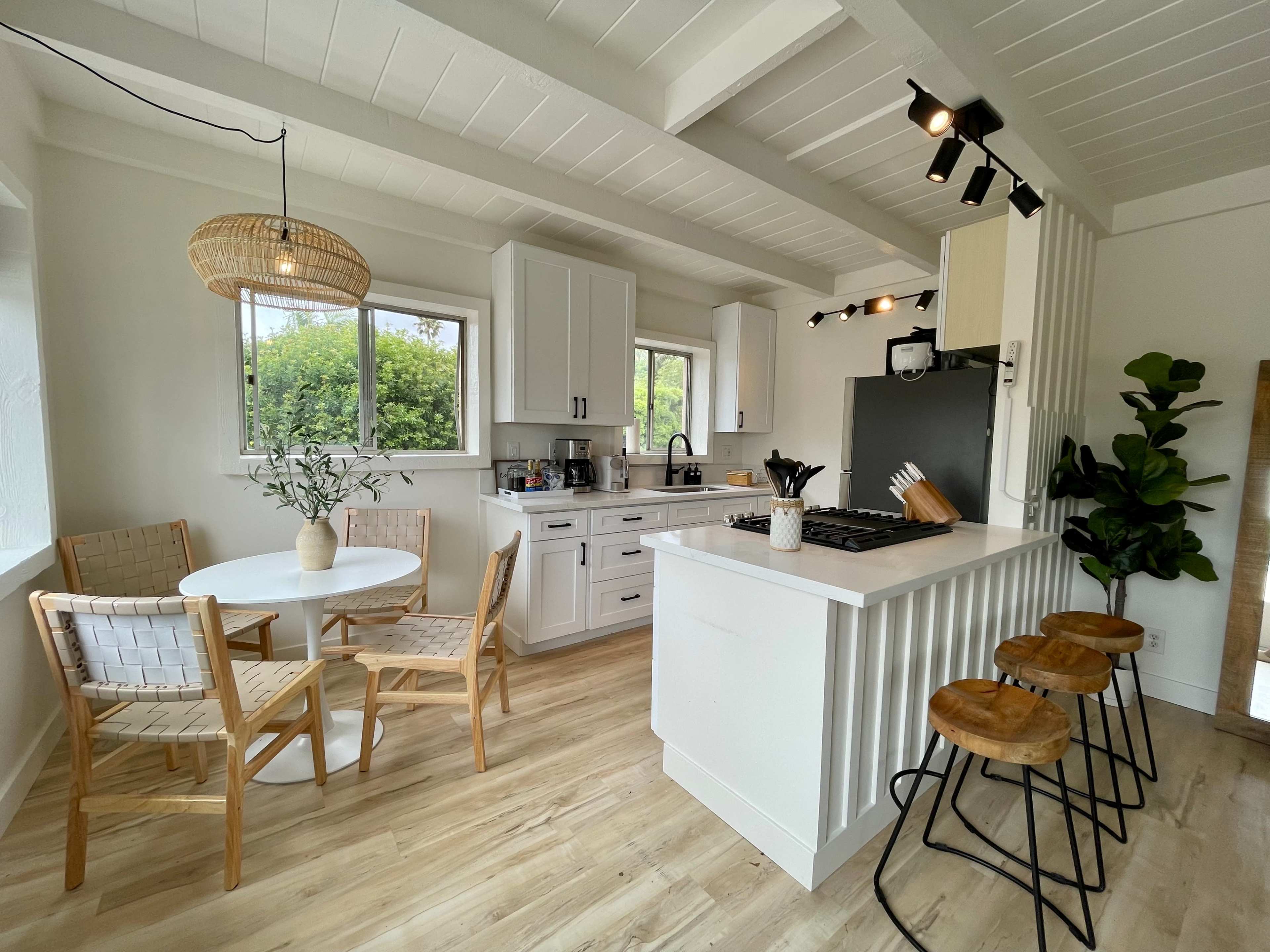 A bright kitchen features white cabinets, a gas stove, a small round dining table with wooden chairs, and bar stools at a counter.