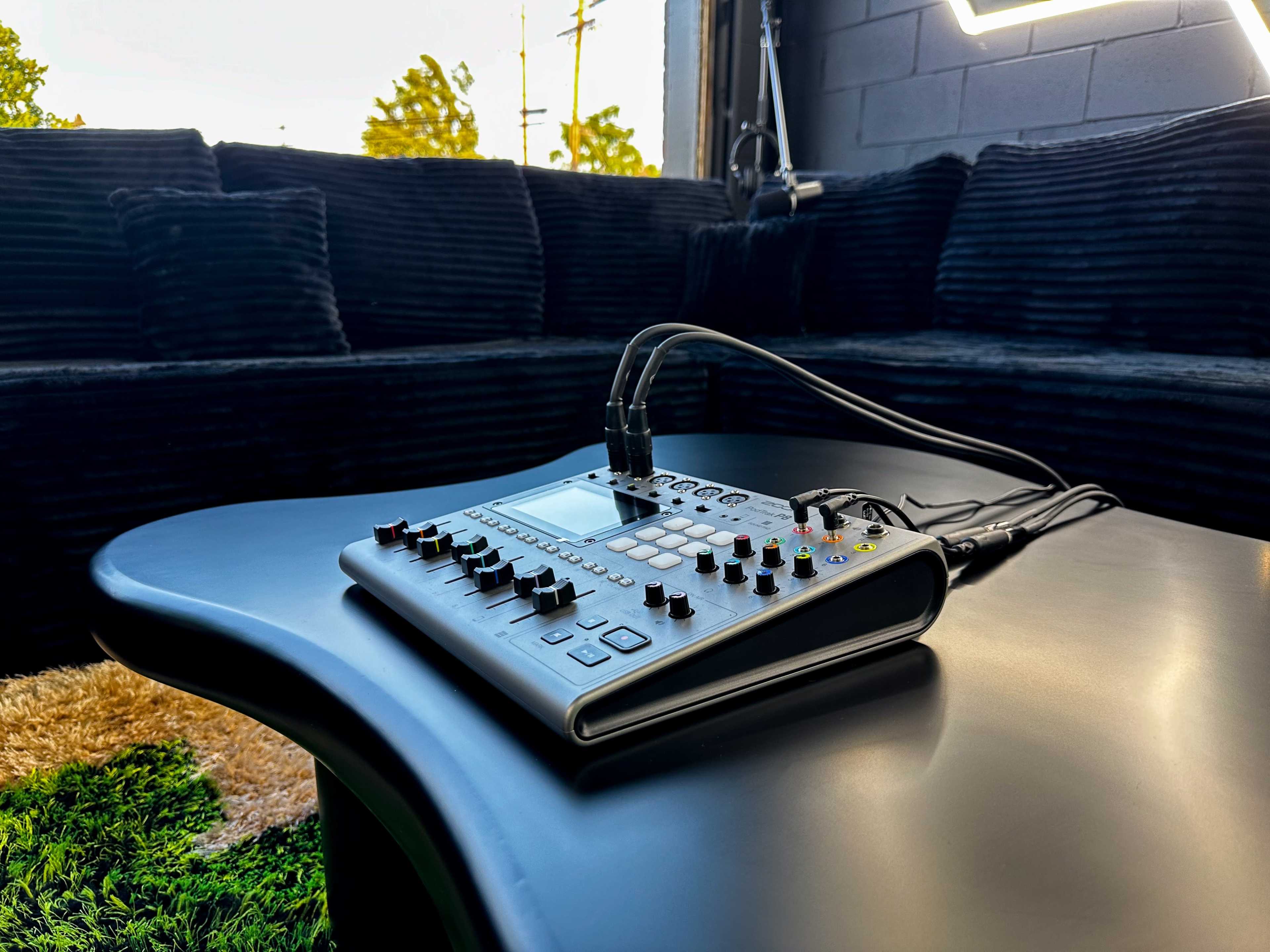 A music production device rests on a black table, with a plush couch and natural light in the background.
