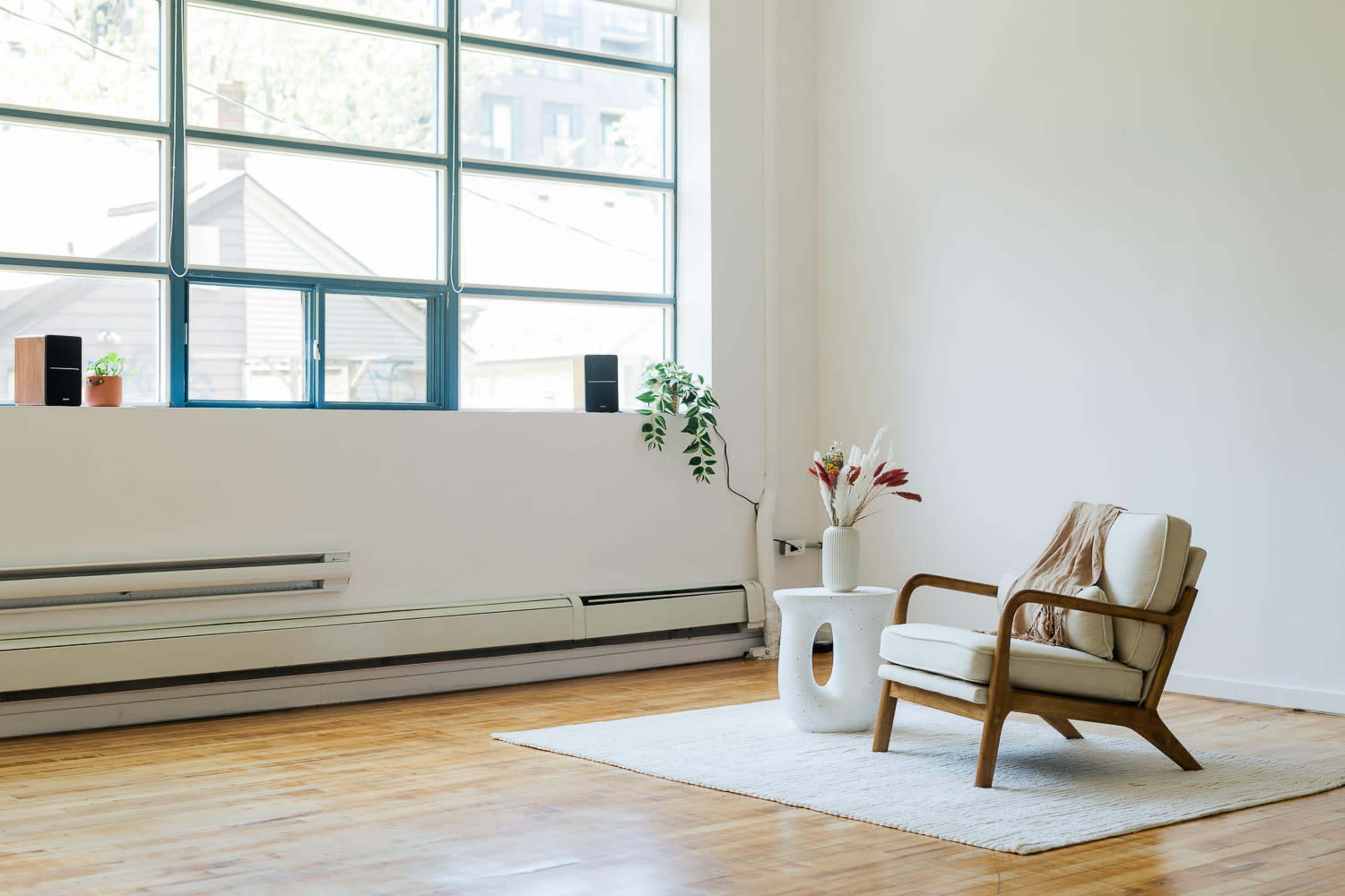 A minimalist room features a wooden chair beside a small white table, with large windows letting in natural light.