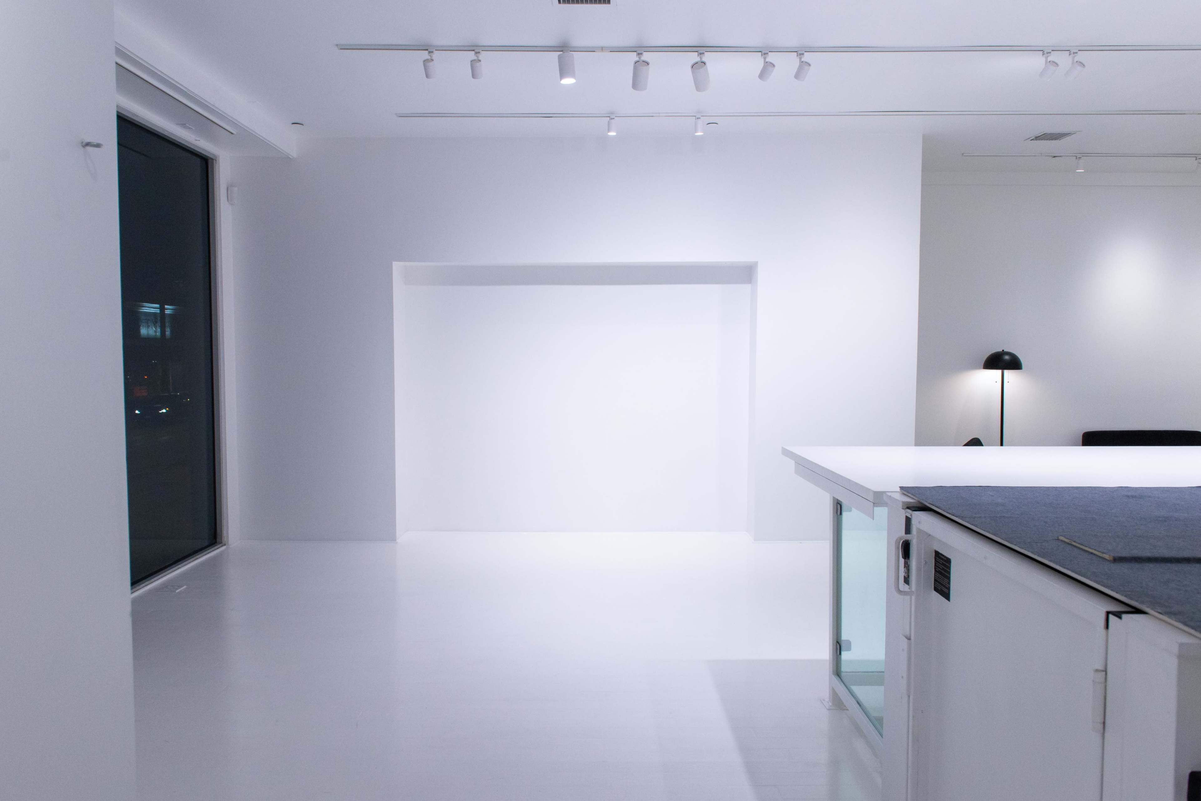 A minimalist, brightly lit interior space with white walls and a large window.