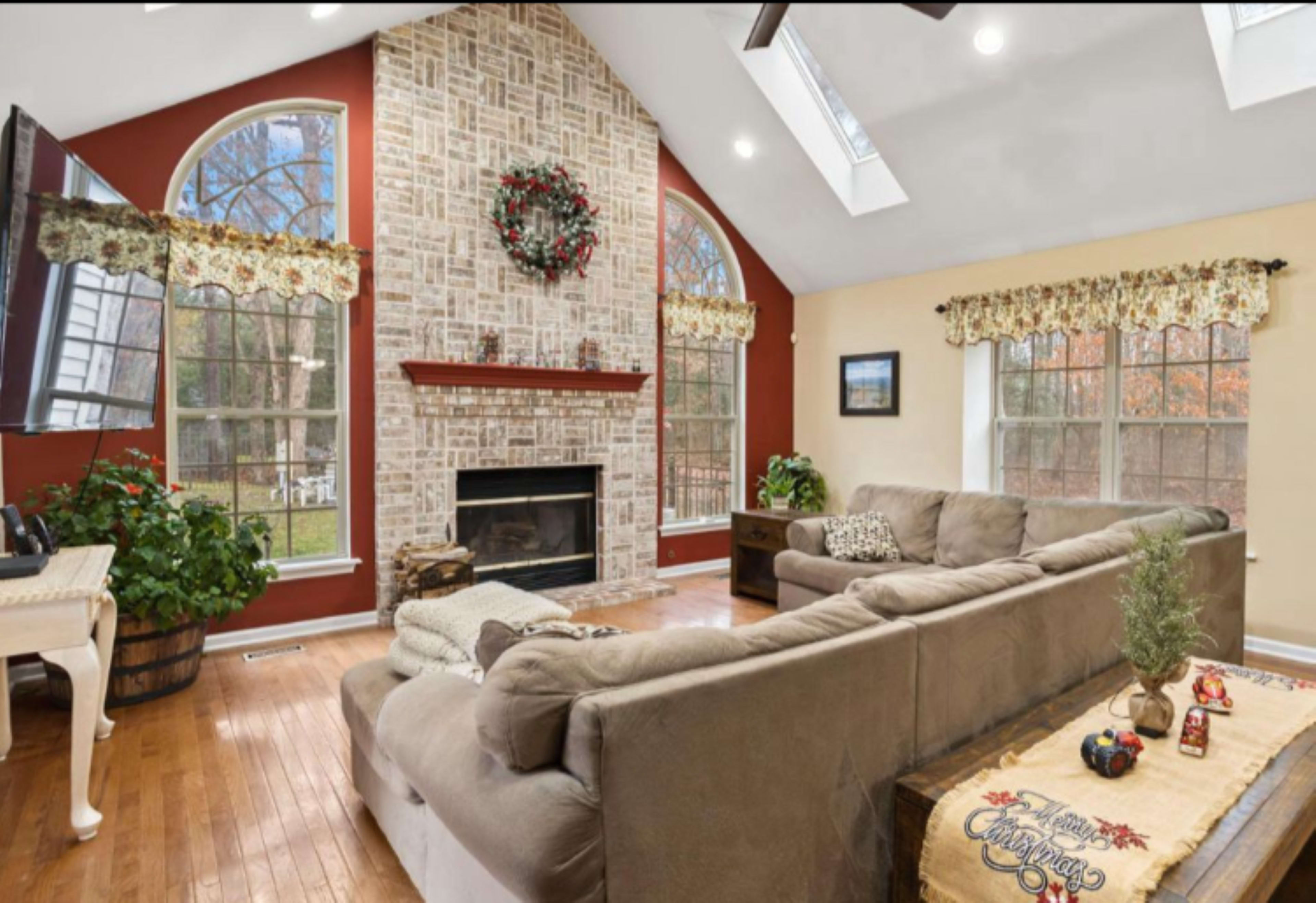The living room features a large sectional sofa, a fireplace with a decorative wreath above it, and tall windows that allow natural light to fill the space.