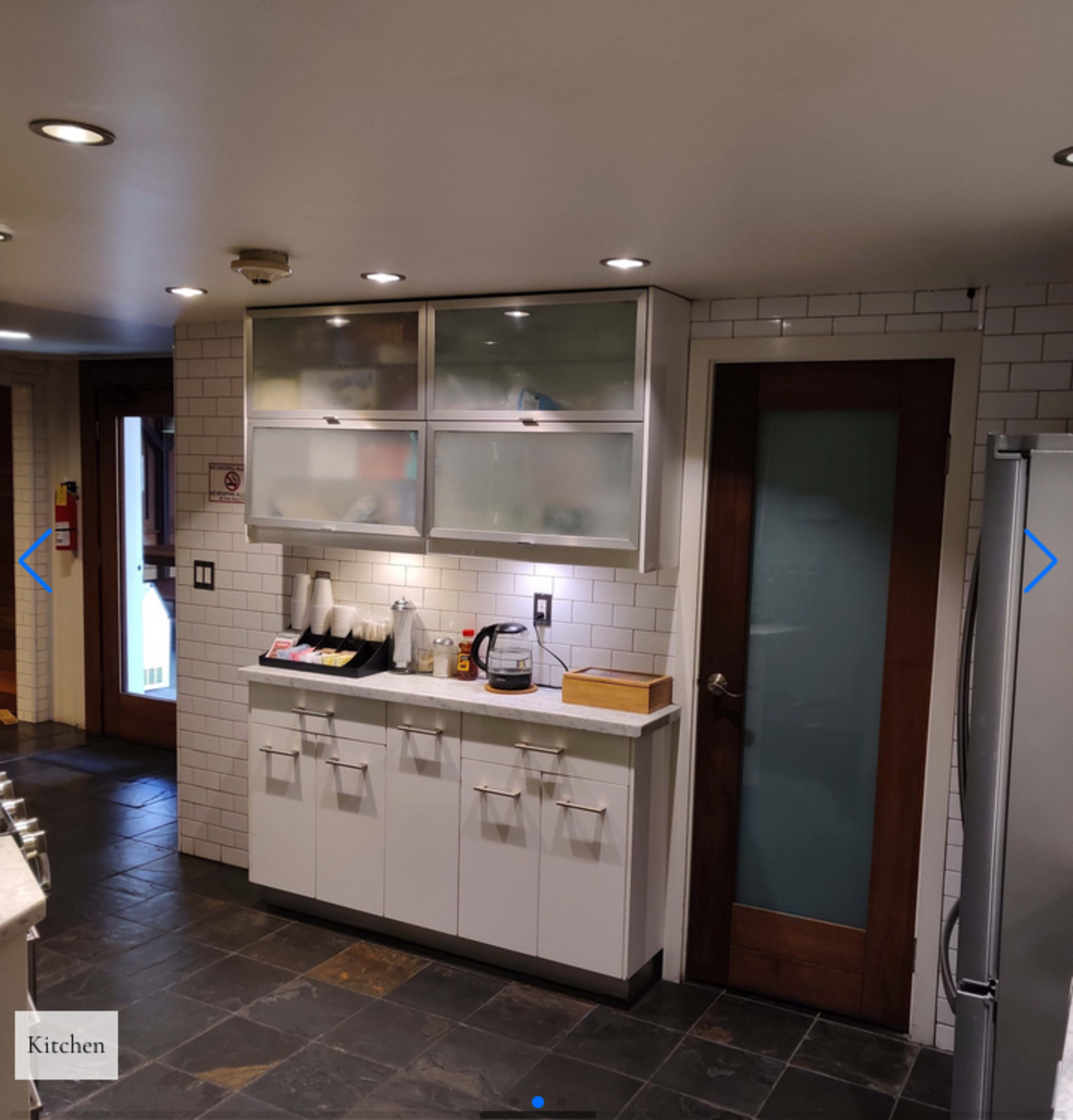 A modern kitchen with white cabinets, a countertop, and a door leading to another room.