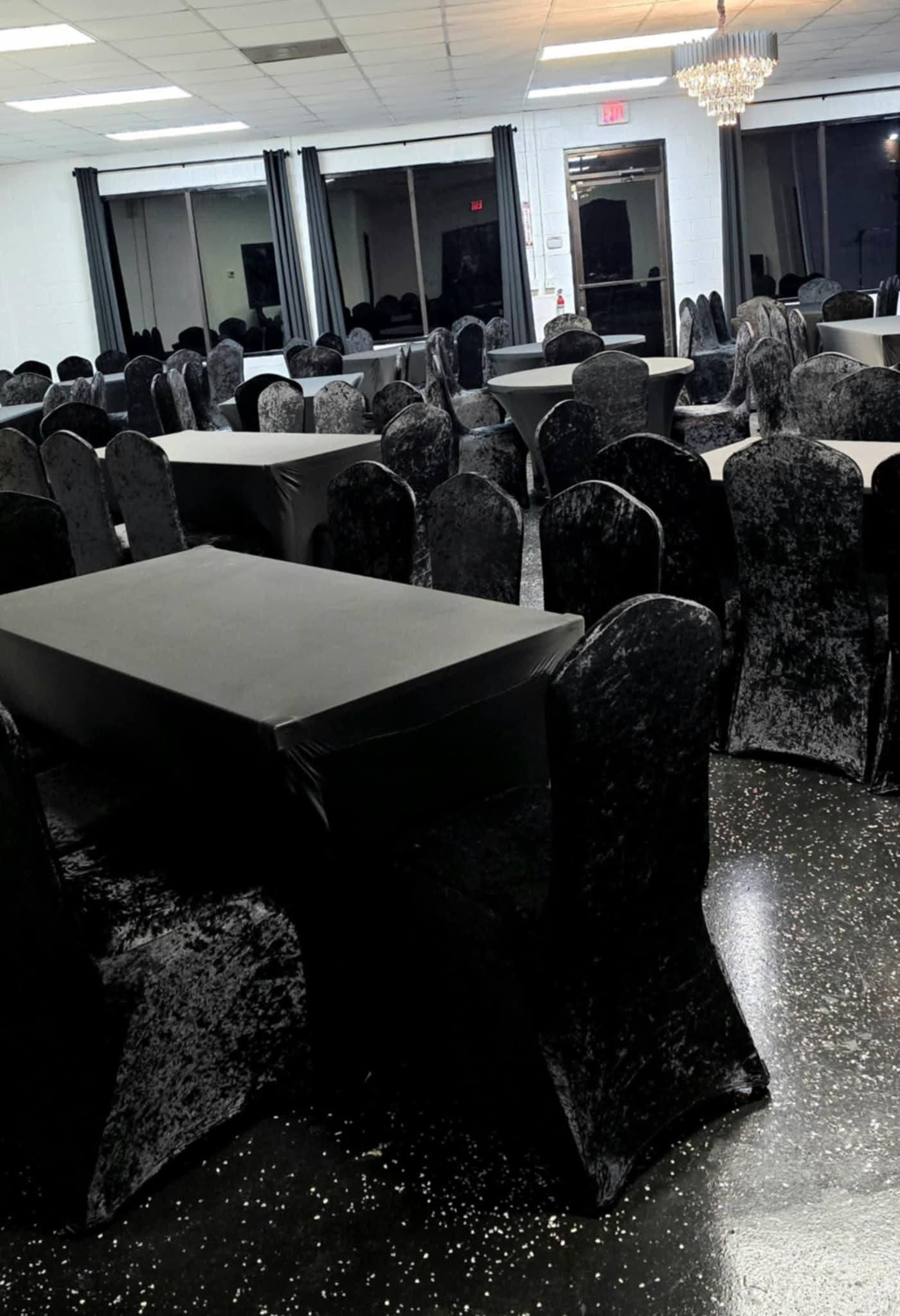 The image shows a spacious event room with numerous black-covered tables and chairs arranged in rows.
