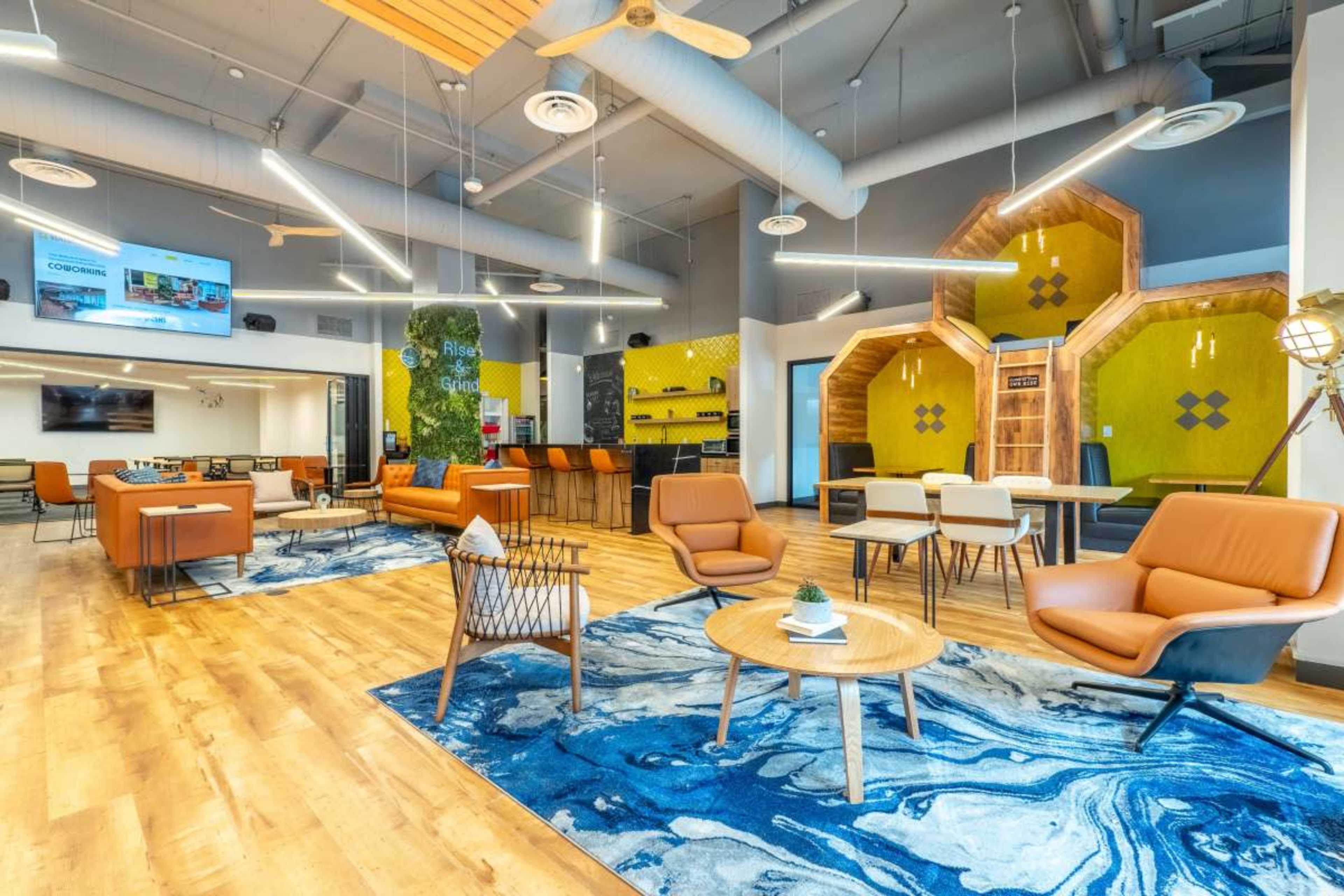 A modern co-working space featuring orange seating, wooden flooring, and a colorful hexagonal wall design.