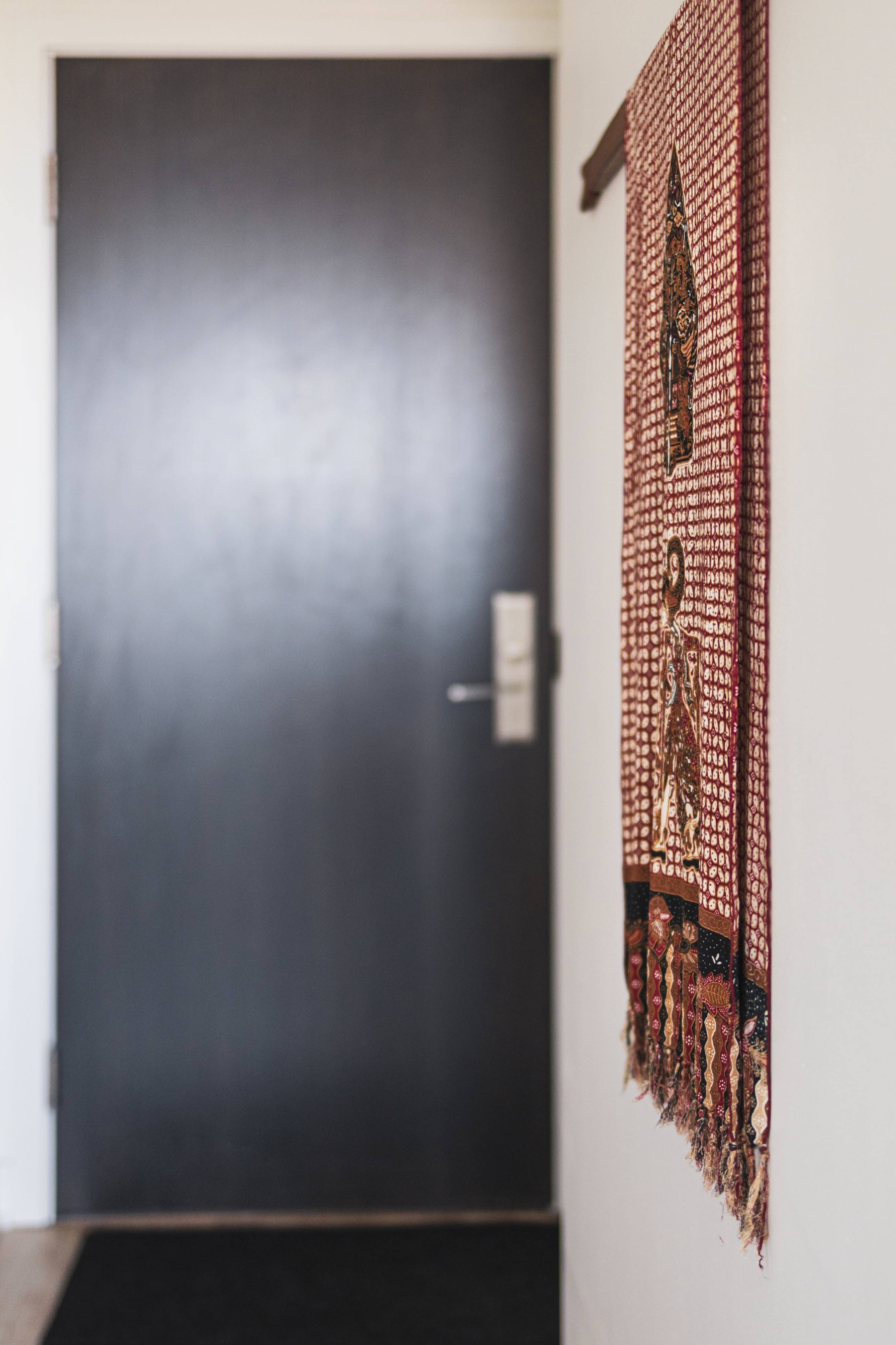 A dark door on one side and a decorative woven wall hanging on the other side near the entrance of a room.