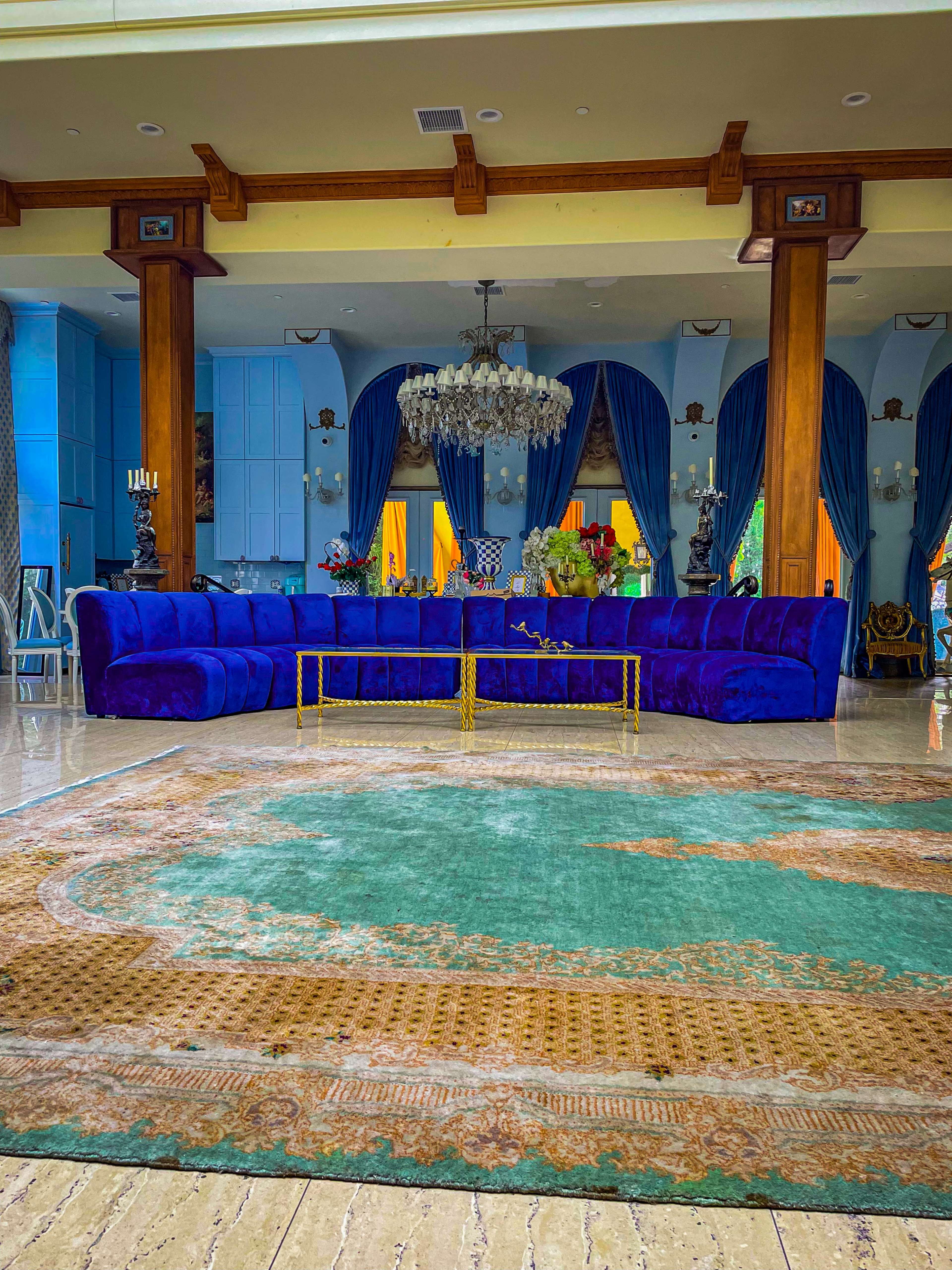 A spacious living area features a large blue sectional sofa surrounded by decorative elements, including a chandelier and a patterned area rug.