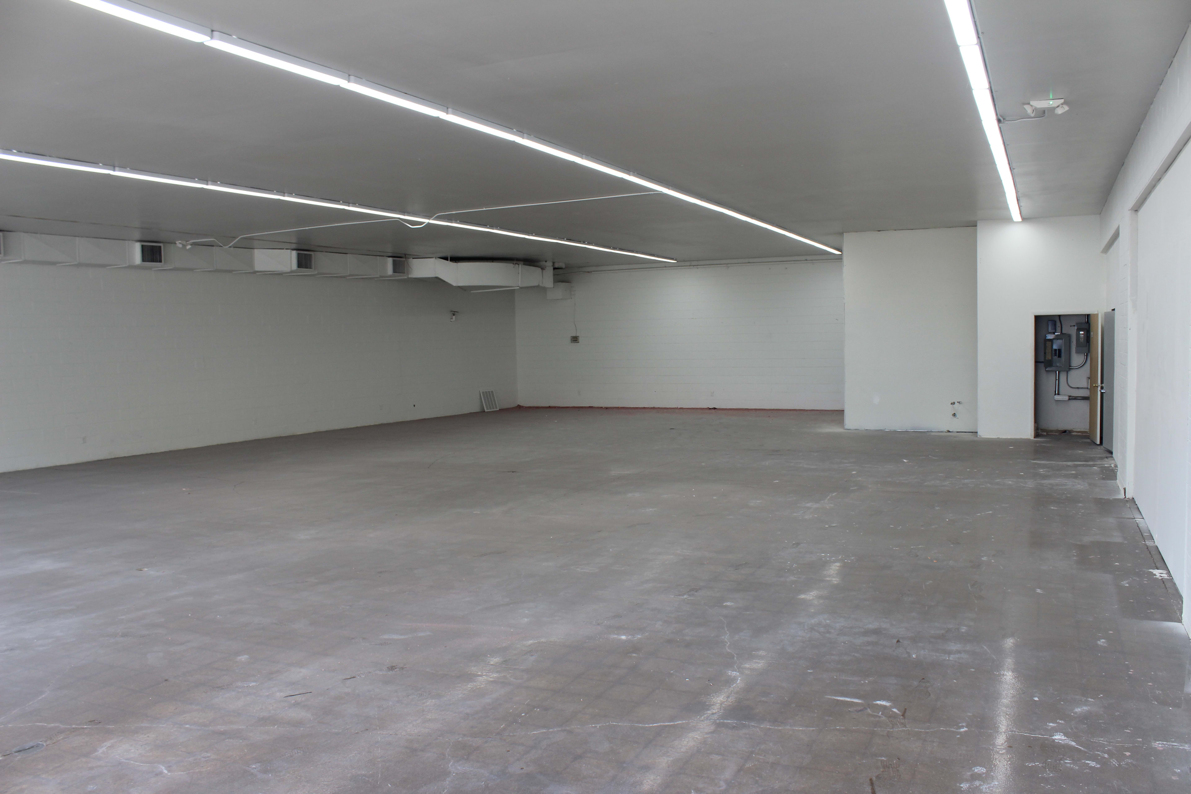 A large, empty commercial space with concrete flooring and flat, white walls.