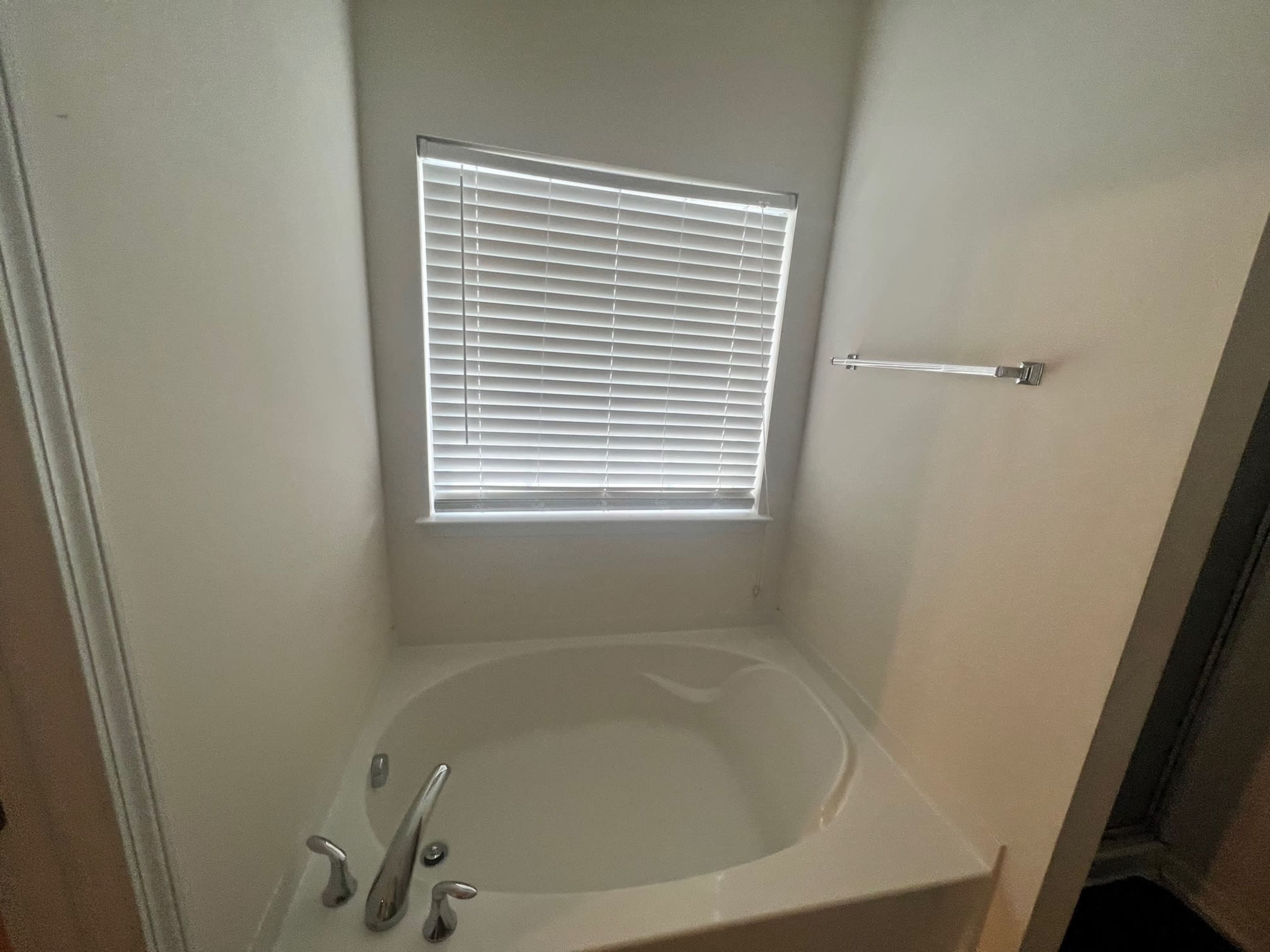A corner of a bathroom featuring a bathtub beneath a window with blinds.