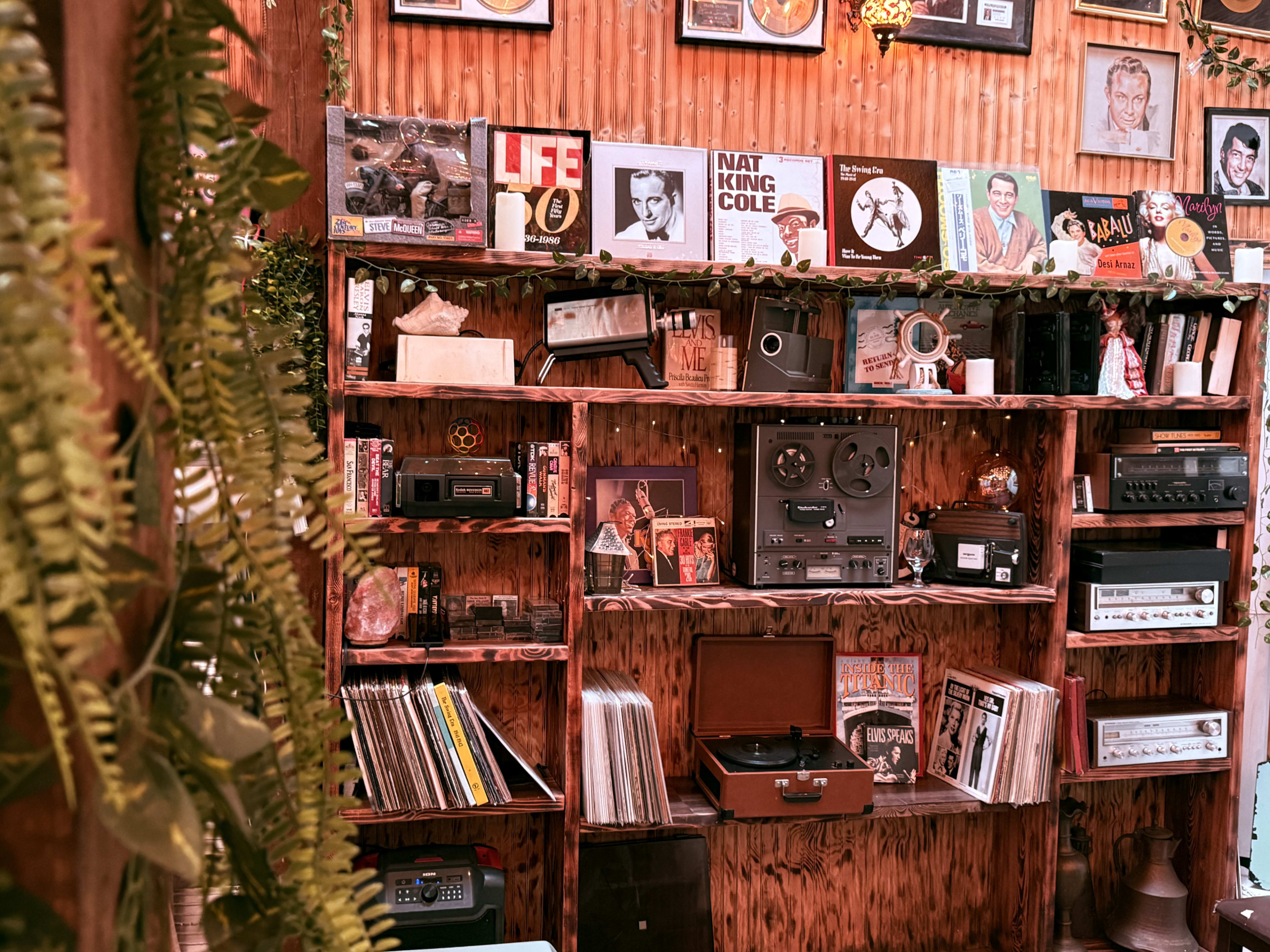The image shows a wooden shelf filled with various vintage audio equipment, vinyl records, and framed photographs.