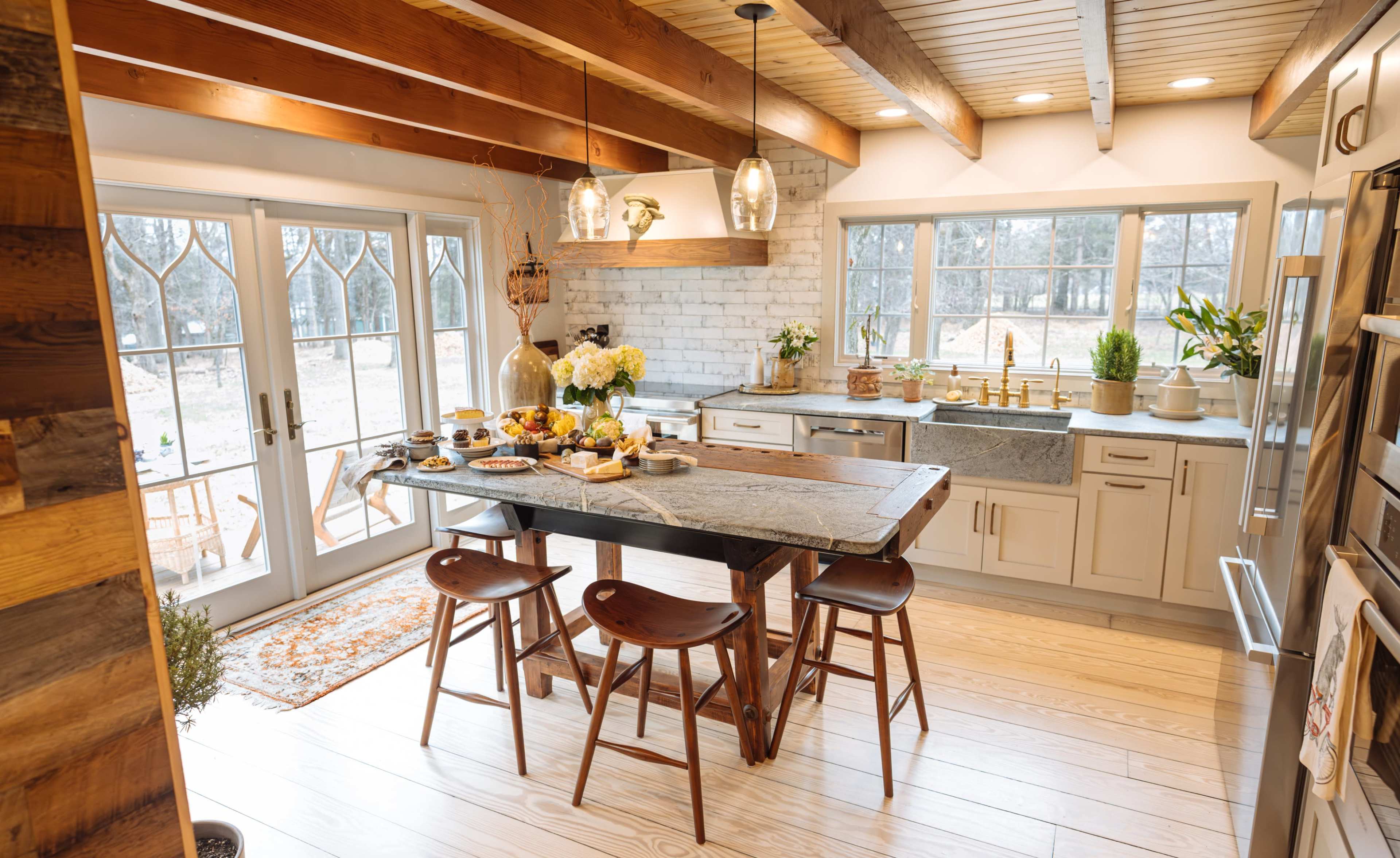 A beautifully designed kitchen features a large wooden table set for a meal, surrounded by chairs, with large windows providing natural light and a view of the outdoors.