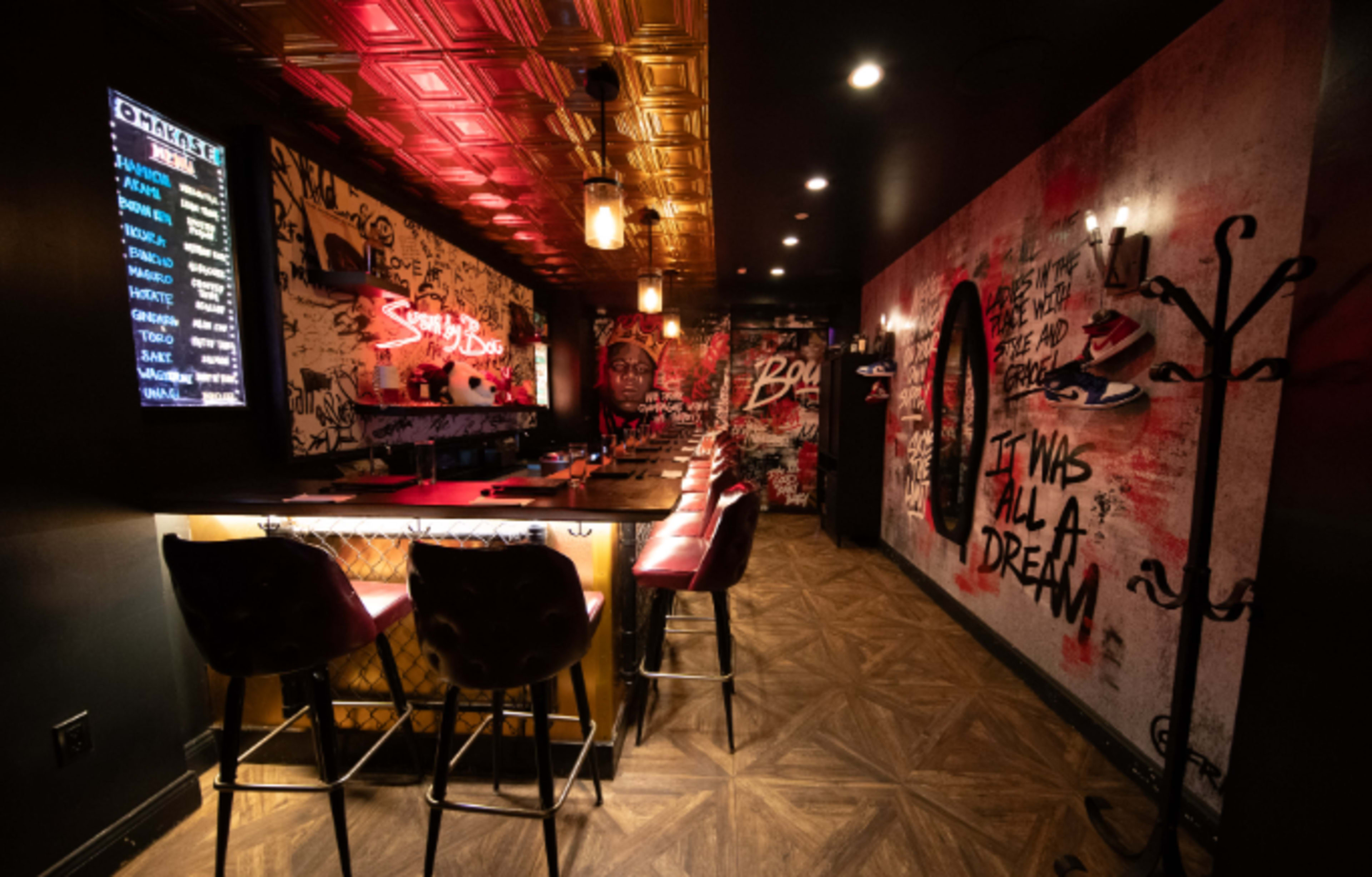 The image shows a stylish bar interior with graffiti art on the walls, accented lighting, and high stools placed around a long bar counter.