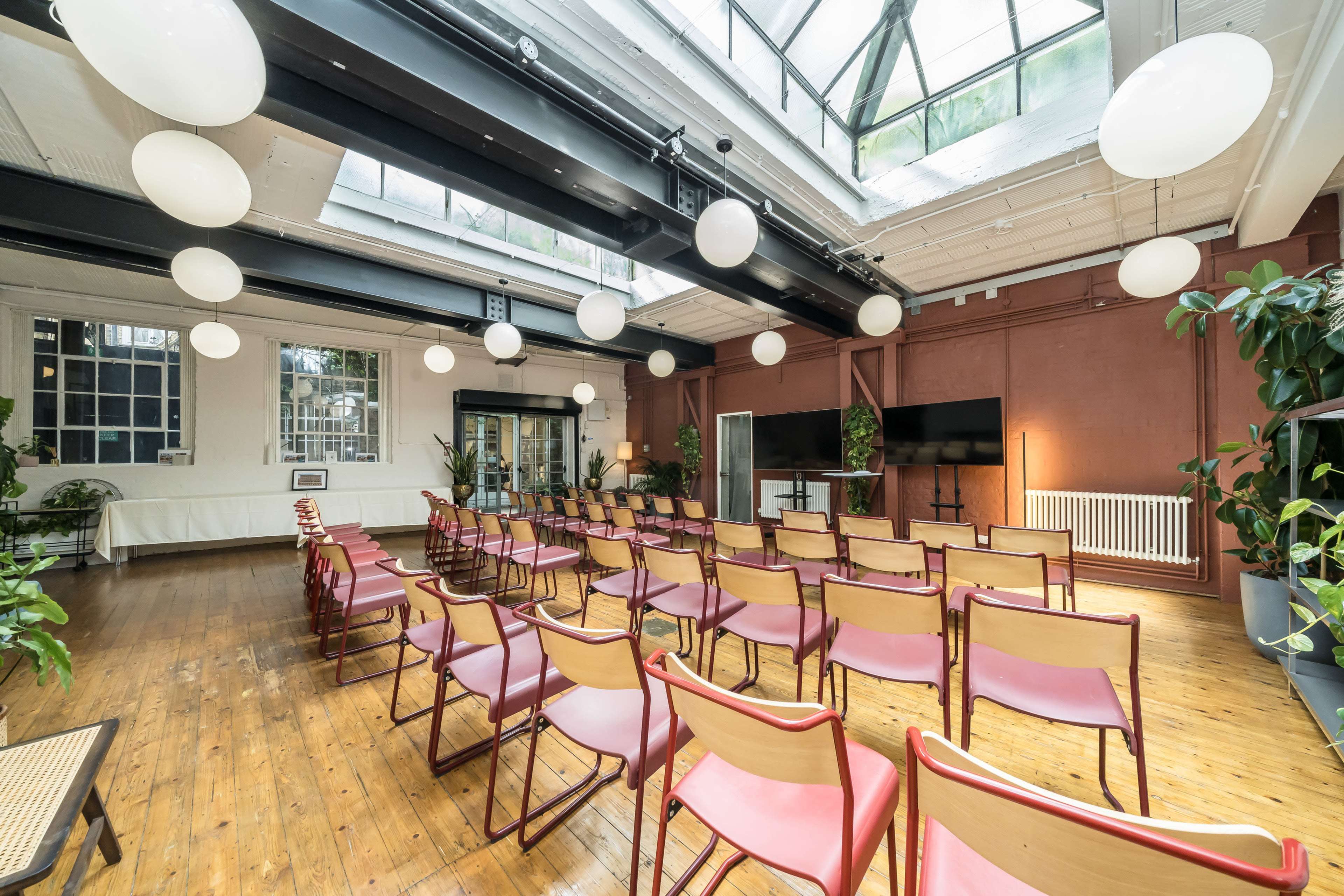 The image shows a spacious event room with wooden floors, rows of chairs, and a large skylight illuminating the space.