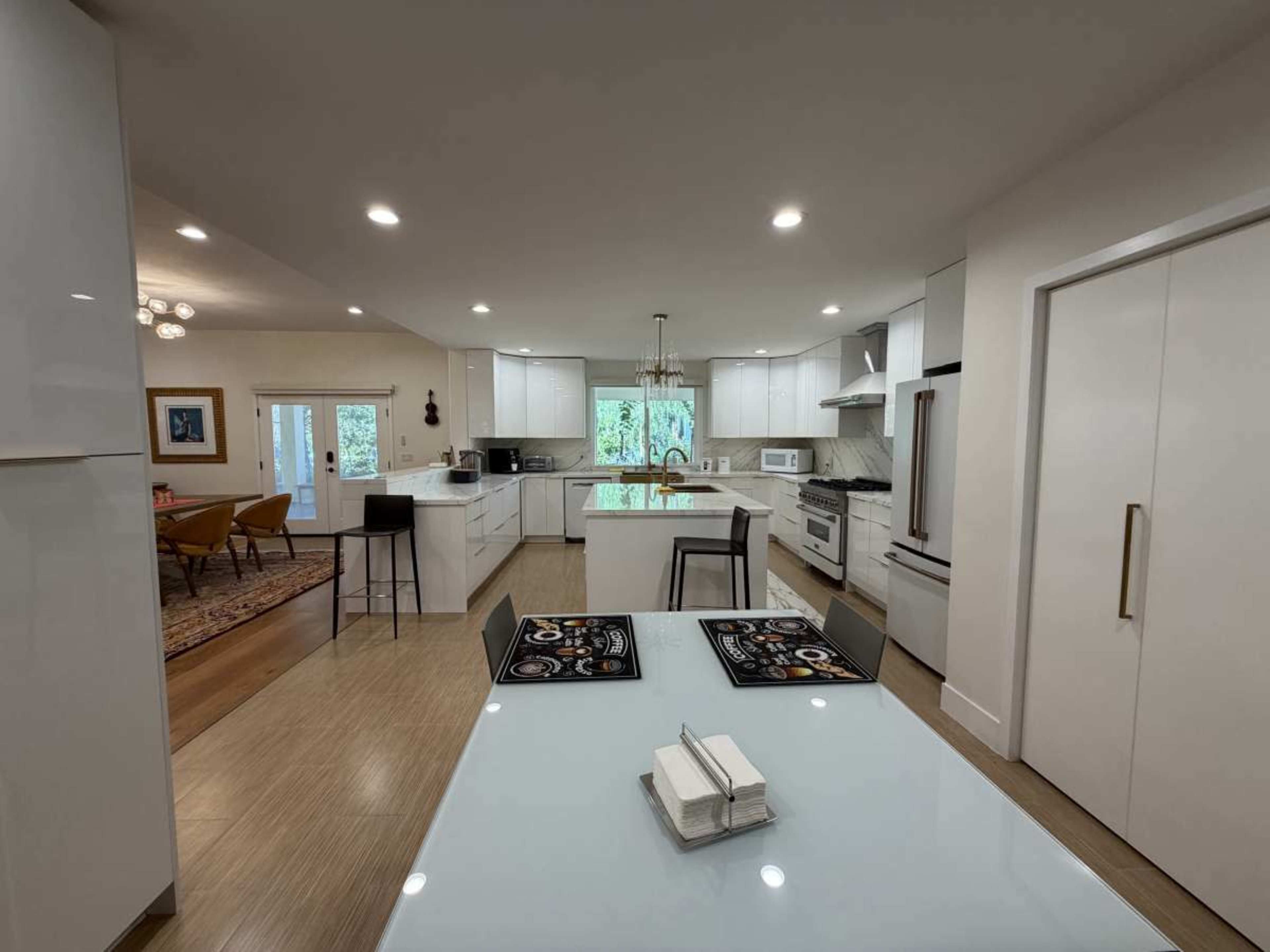 The image shows a modern kitchen with white cabinetry, a central island, and an open layout that connects to a dining area.