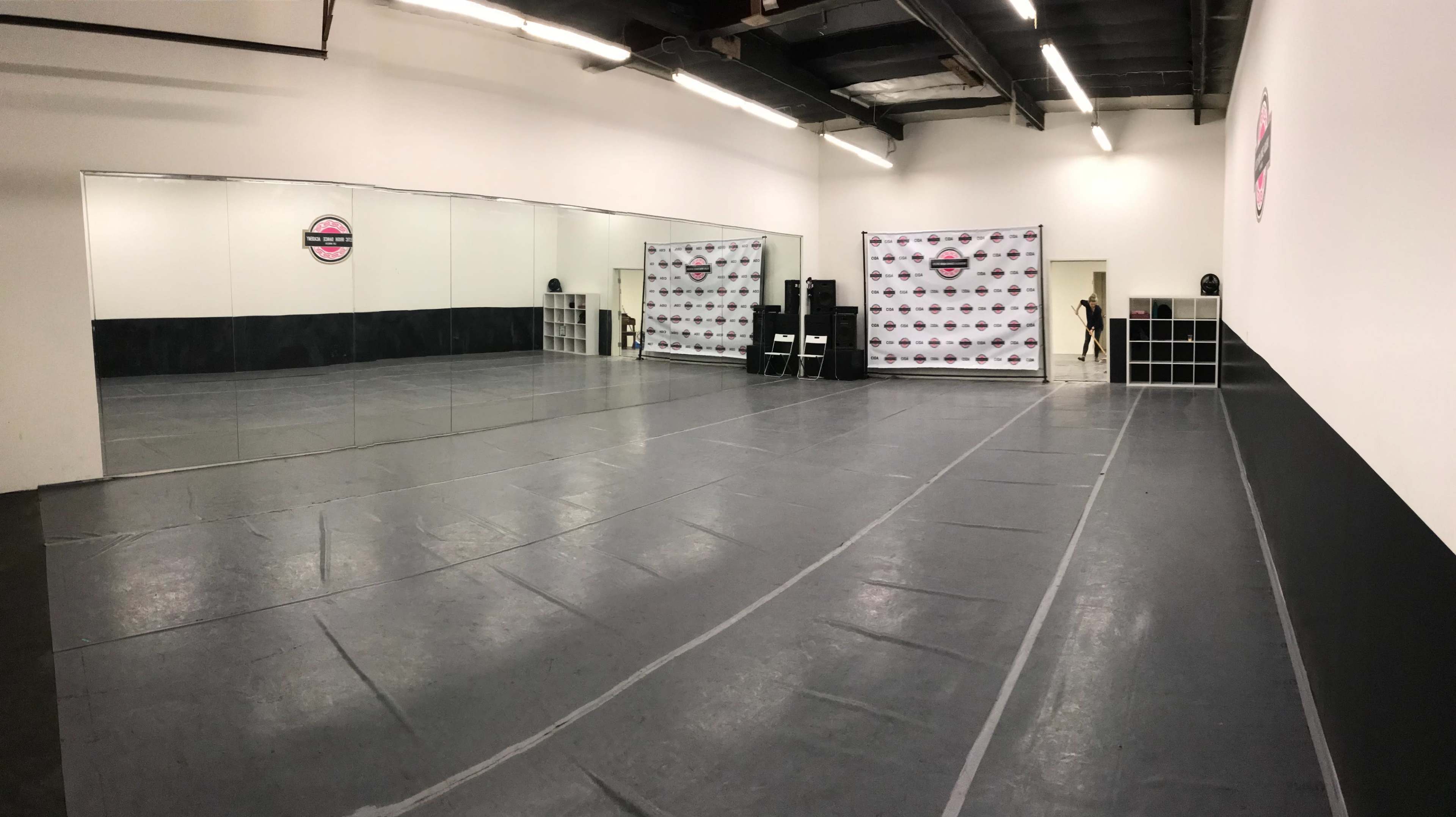 The image shows a spacious dance studio with mirrors on one wall and a promotional backdrop against another wall.