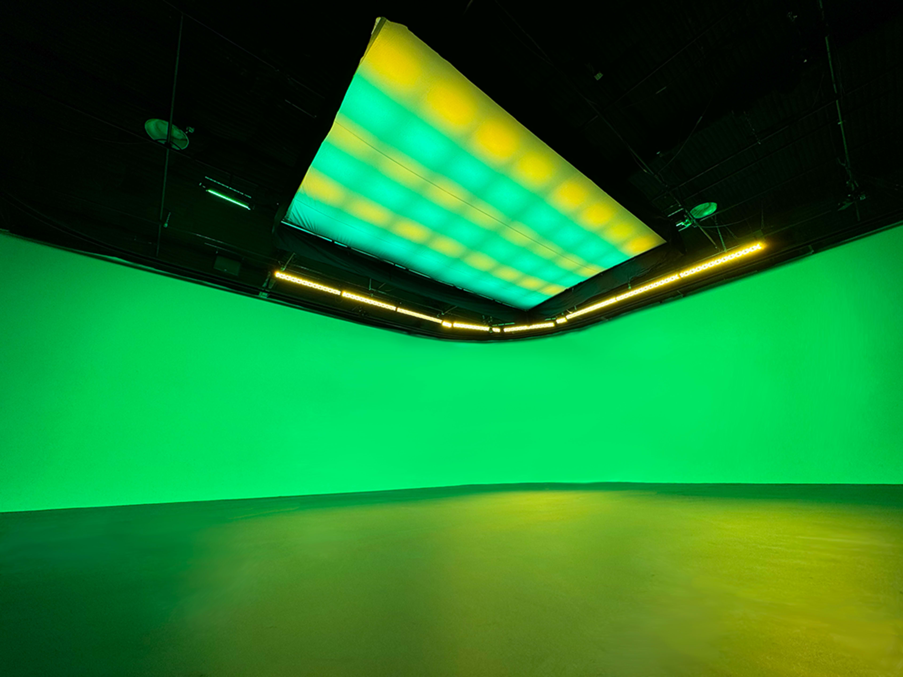 A spacious studio with a green backdrop and a brightly lit ceiling.