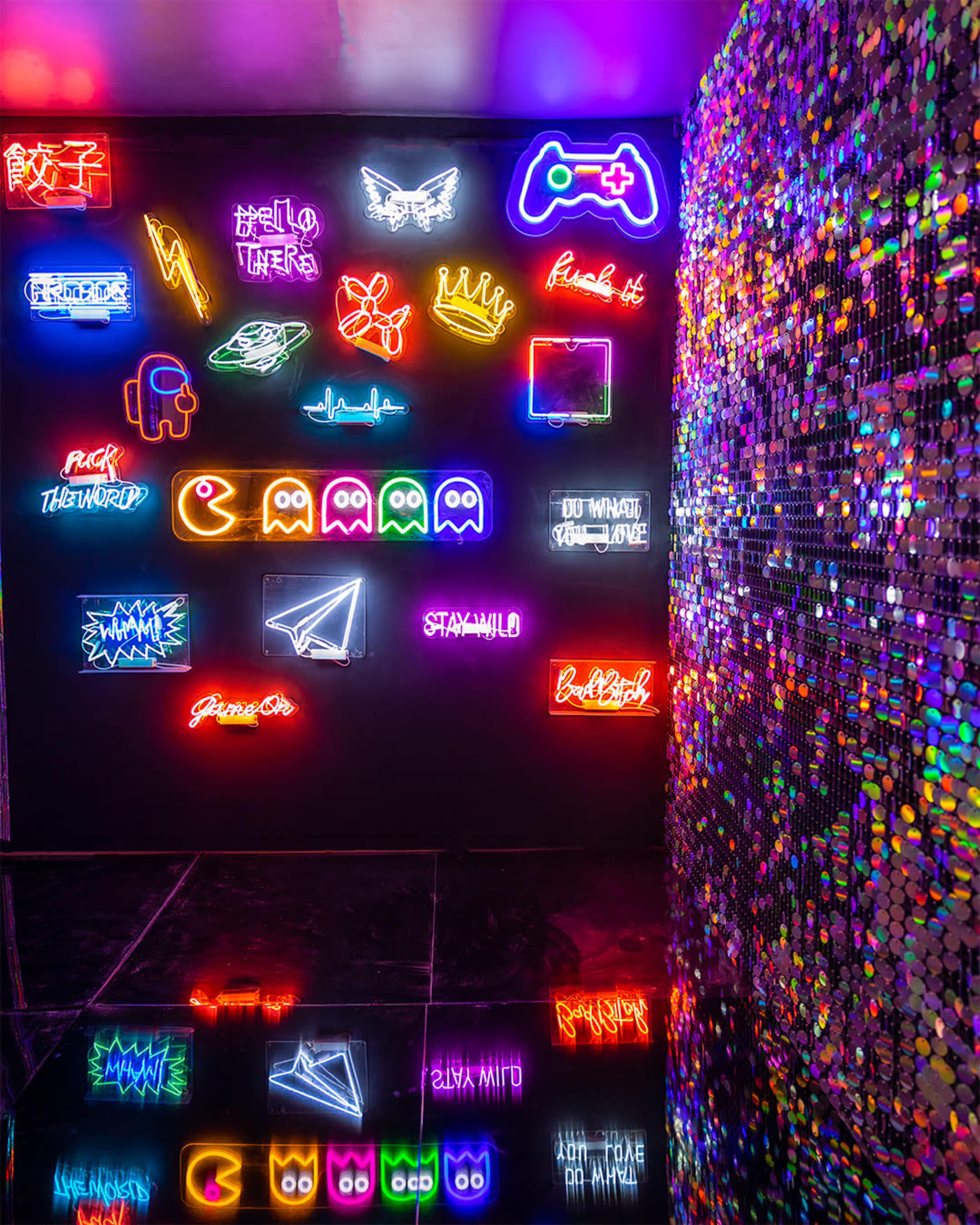 A wall decorated with various neon signs and a glittering, sequined wall on the right.