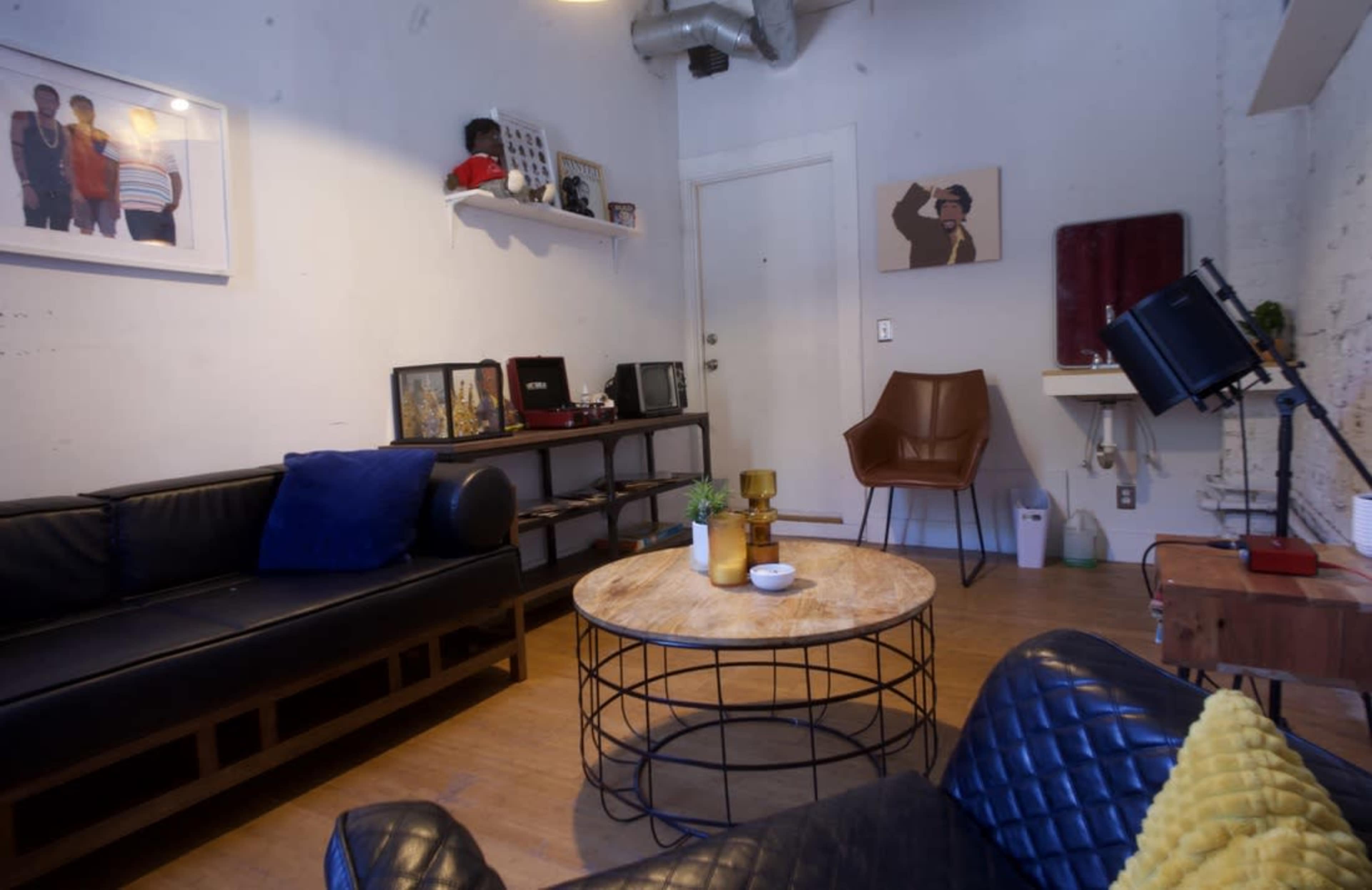 A living room with black leather sofas, a round coffee table, and a wall adorned with framed photos and artwork.