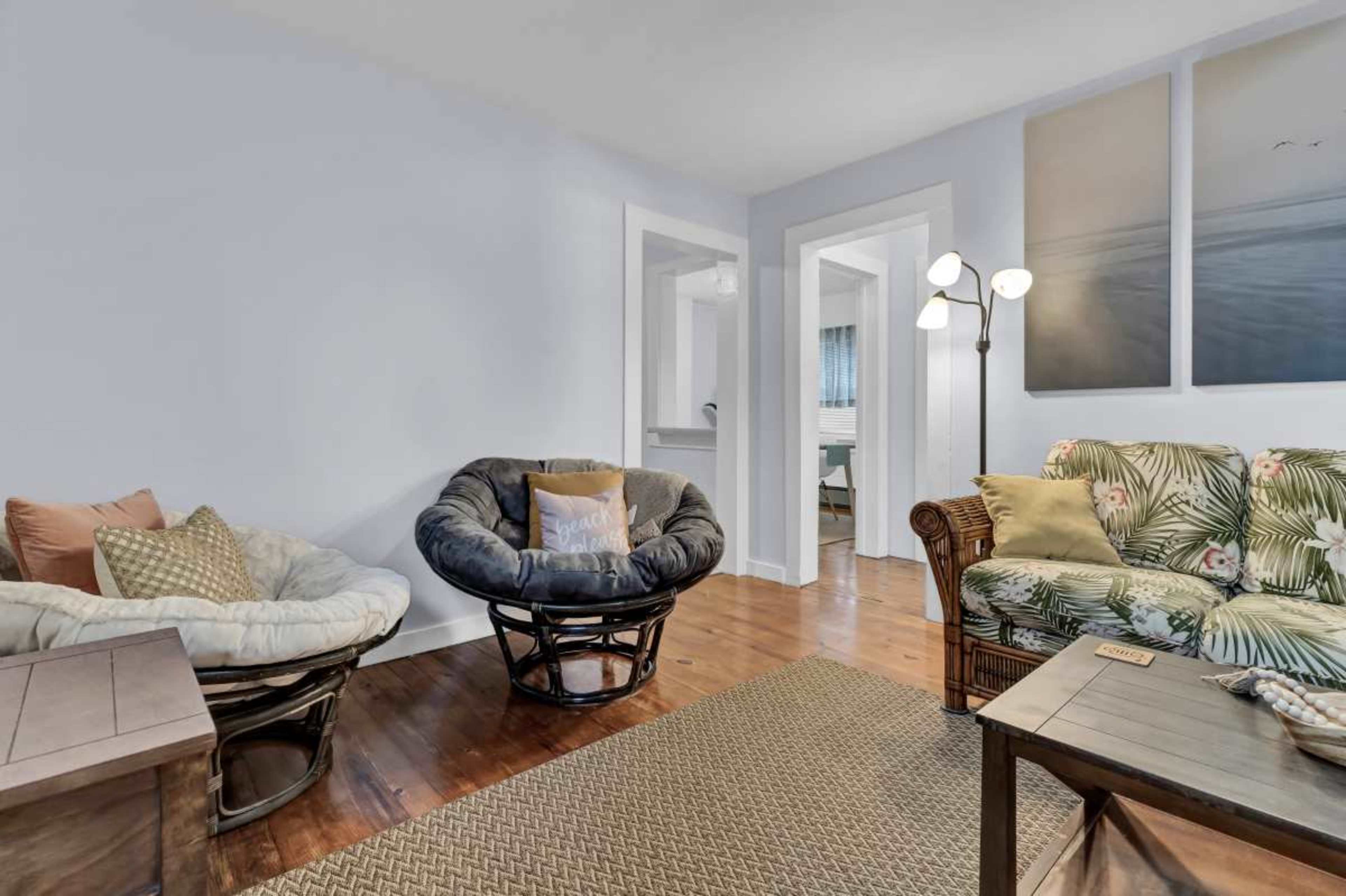 The image shows a living room with two circular chairs, a patterned couch, a wooden table, and light blue walls.