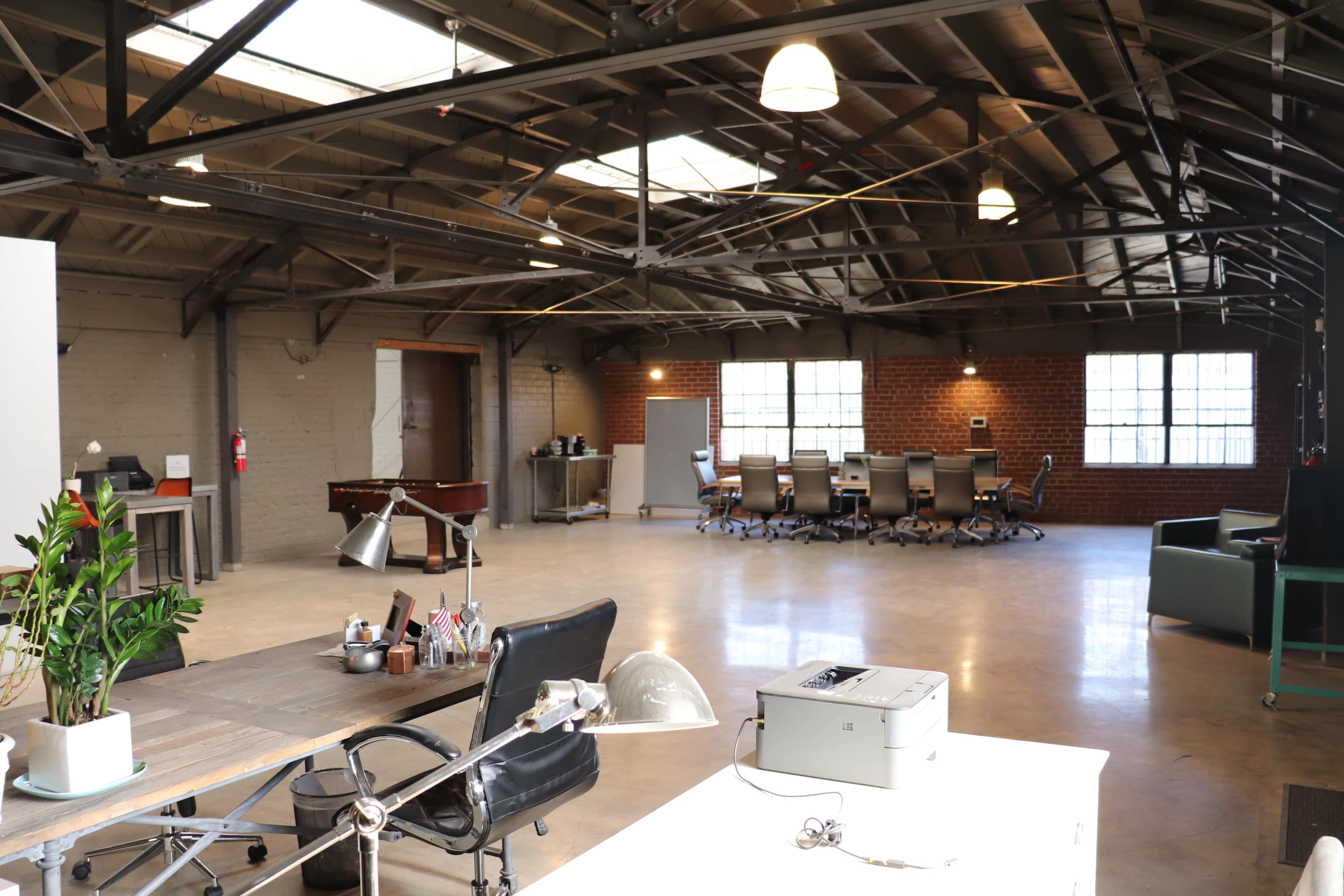 A spacious industrial-style office with high ceilings, a conference area, and various workstations.