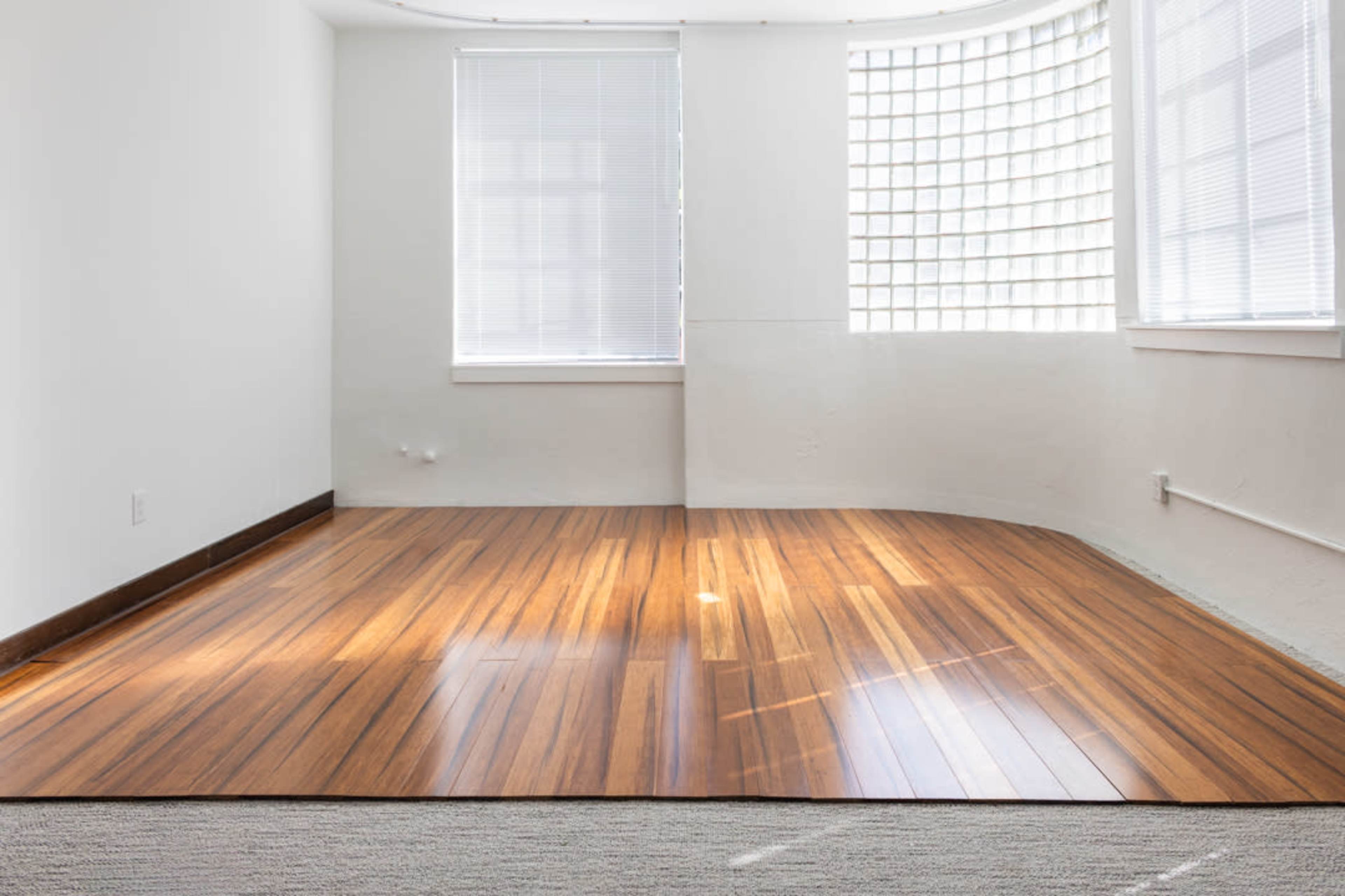 The image shows a spacious room with a wooden floor and large windows allowing natural light to enter.
