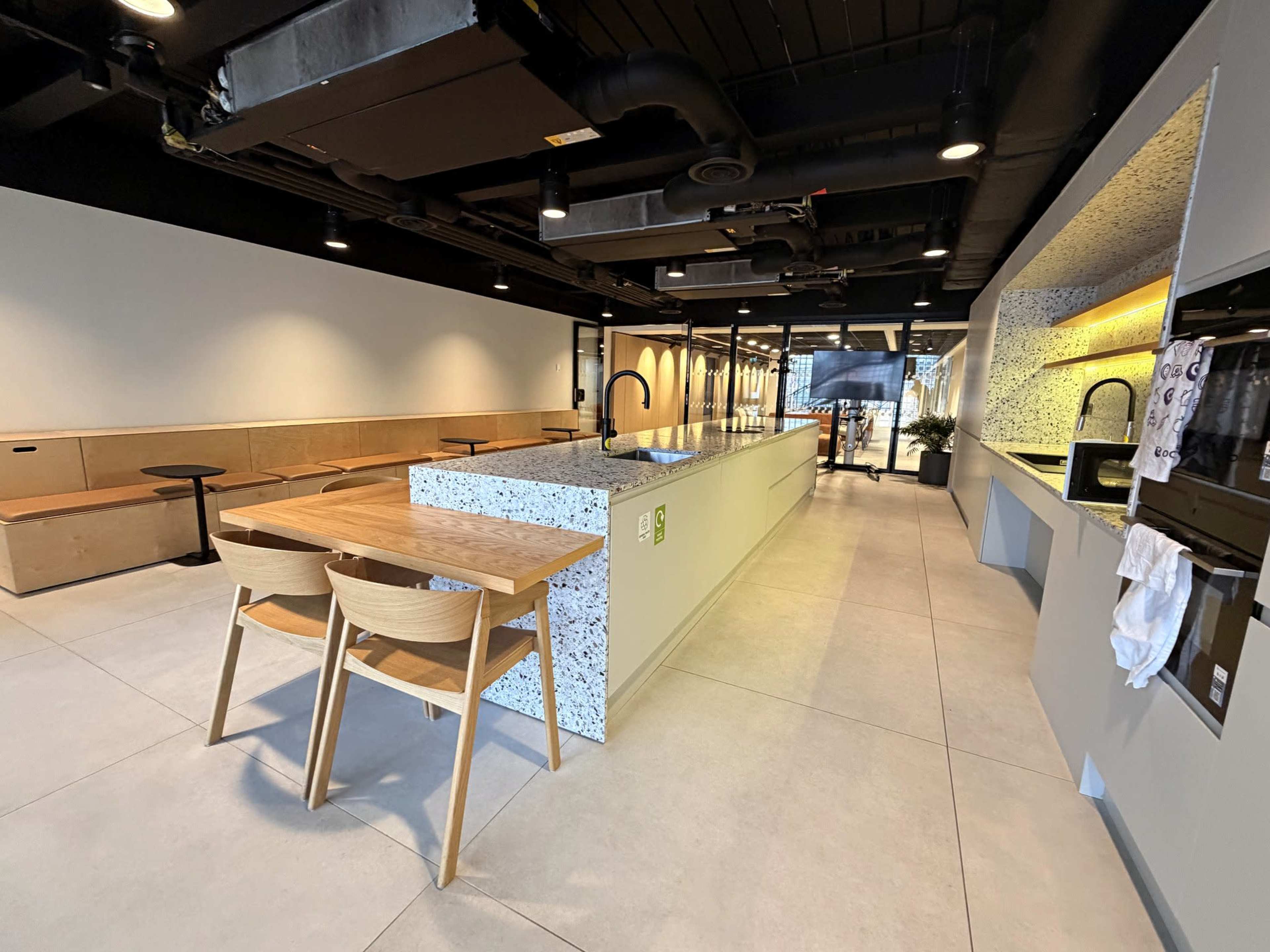 The image shows a modern kitchen space featuring a large island with a textured surface, surrounded by wooden chairs, and an open layout with minimalist decor.